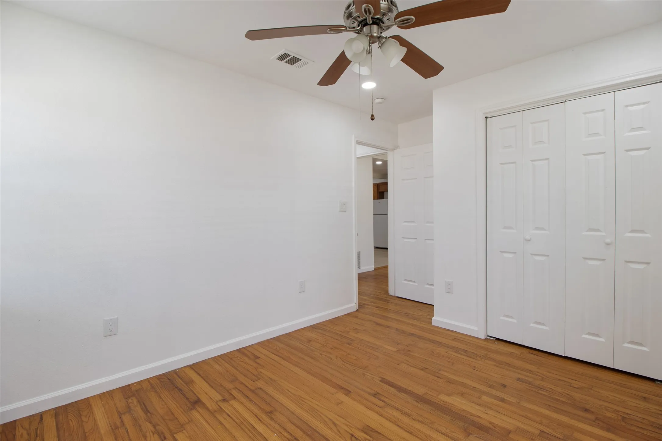 Unfurnished bedroom featuring wood finished floors, ceiling fan, a closet, and freestanding refrigerator