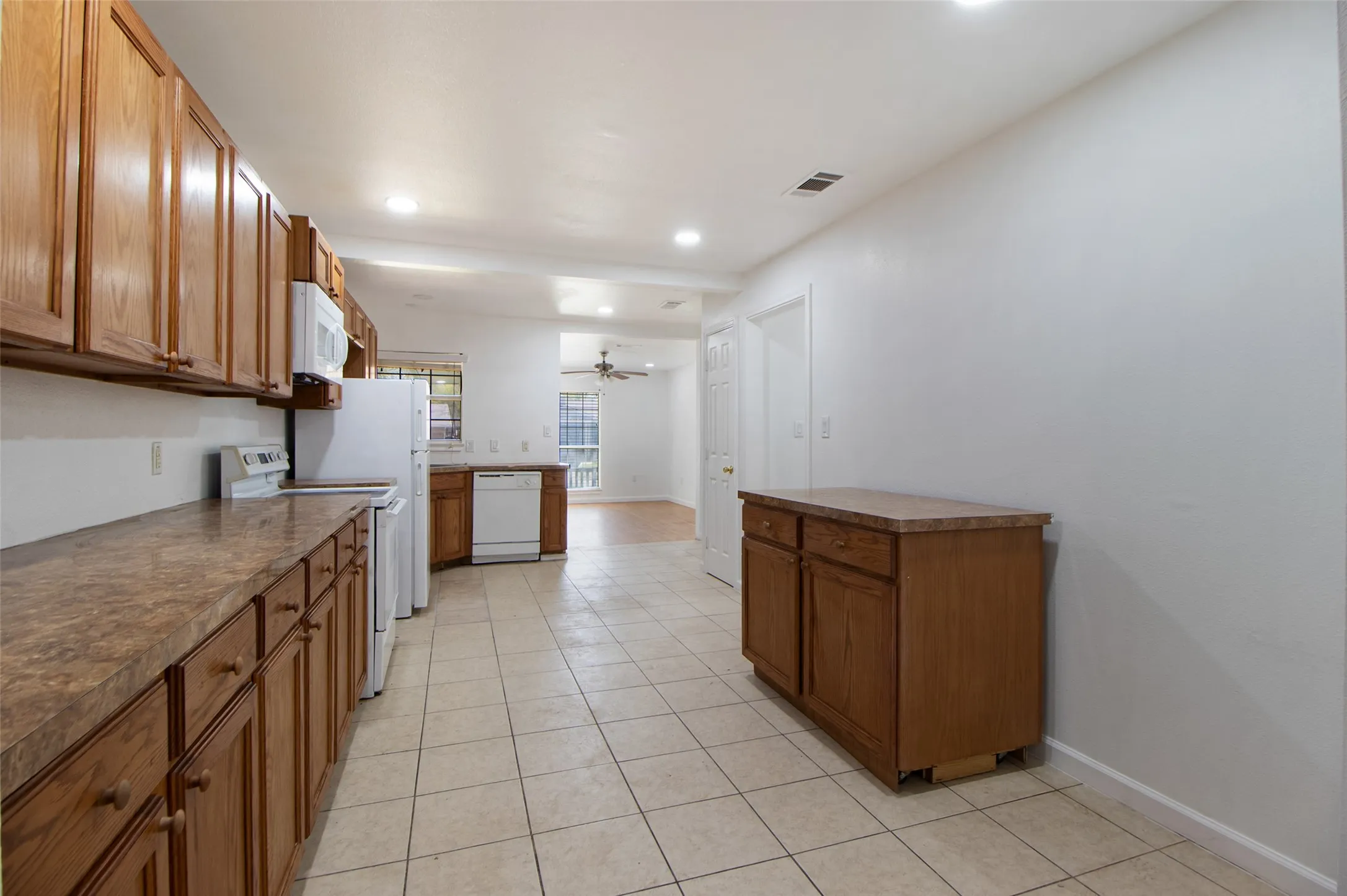 Kitchen featuring wood finish cabinetry, white appliances, light tile patterned floors, dark countertops, and recessed lighting
