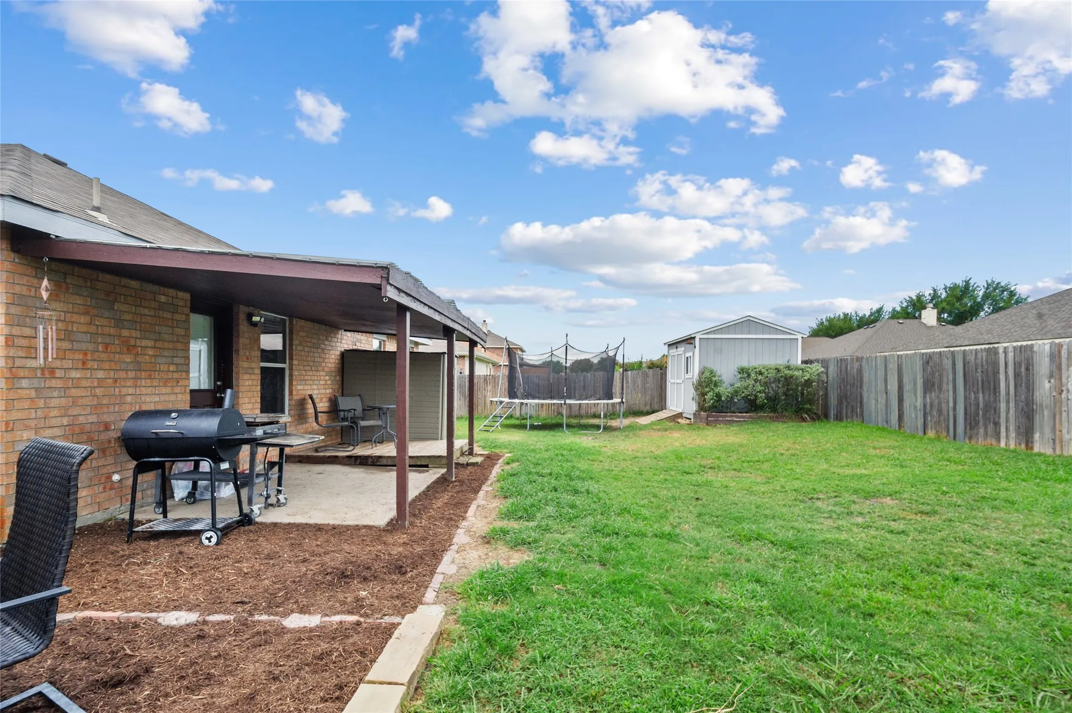 Fenced backyard featuring a trampoline, a patio, and a storage unit