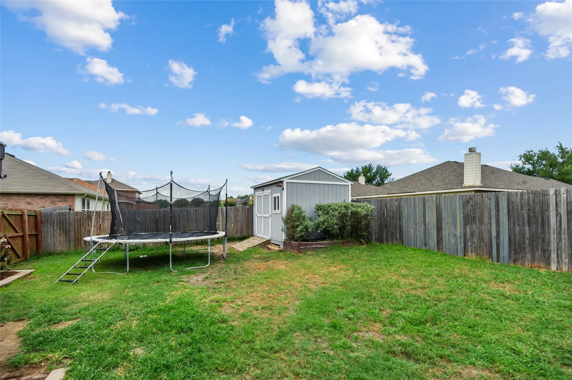 Fenced backyard featuring a trampoline and a storage shed