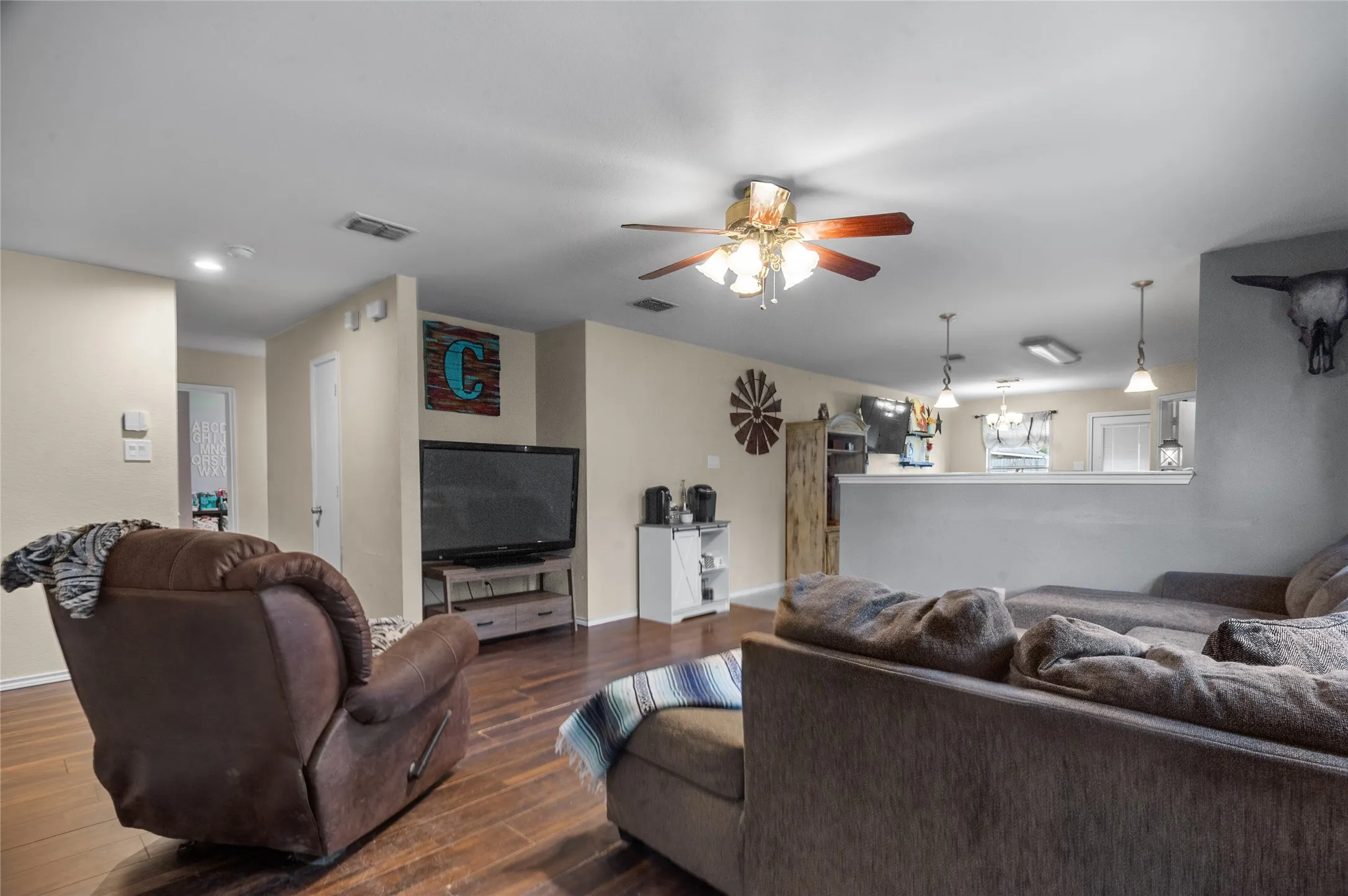 Living room featuring ceiling fan, dark wood-style flooring, and a chandelier