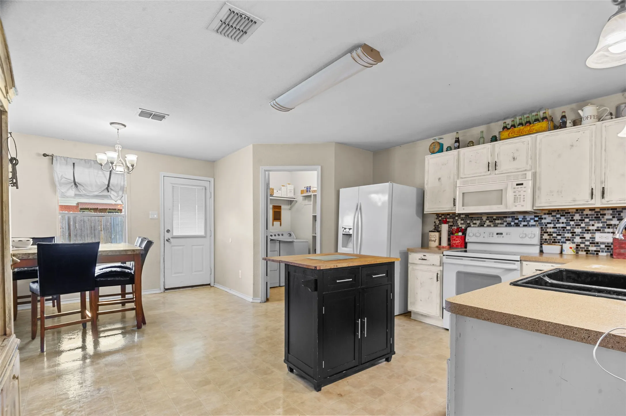 Kitchen featuring white appliances, dark cabinetry, a chandelier, light floors, and washing machine and dryer