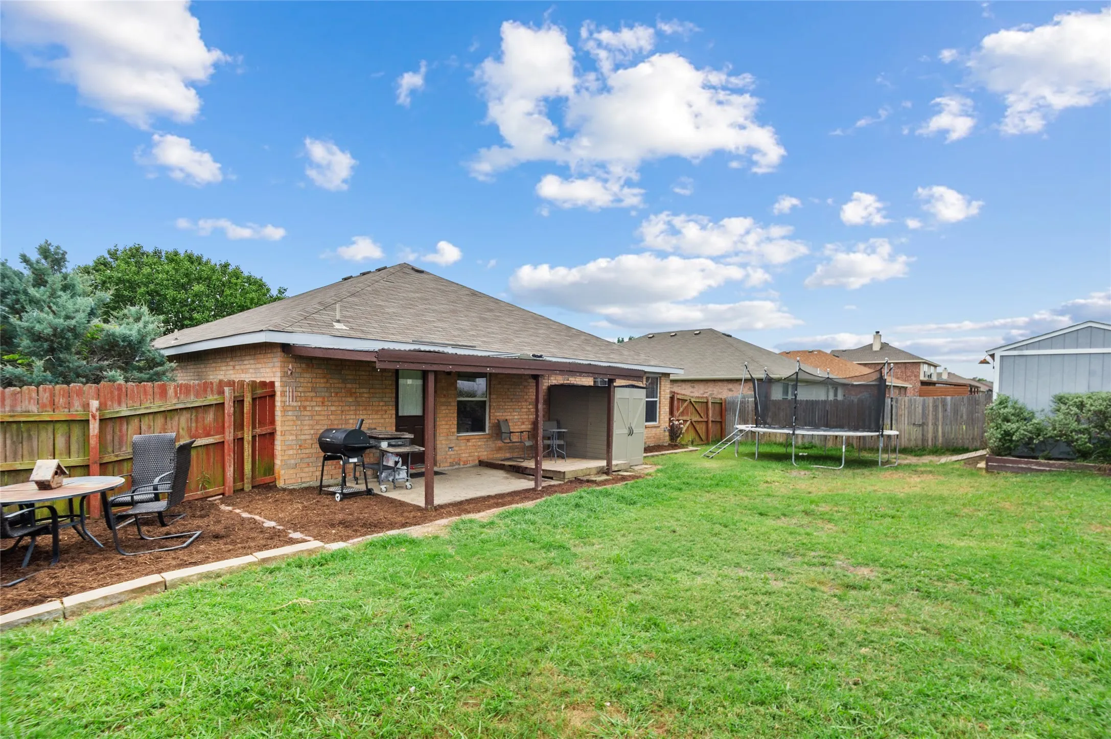 Rear view of property featuring a trampoline, a patio, a fenced backyard, brick siding, and a shingled roof