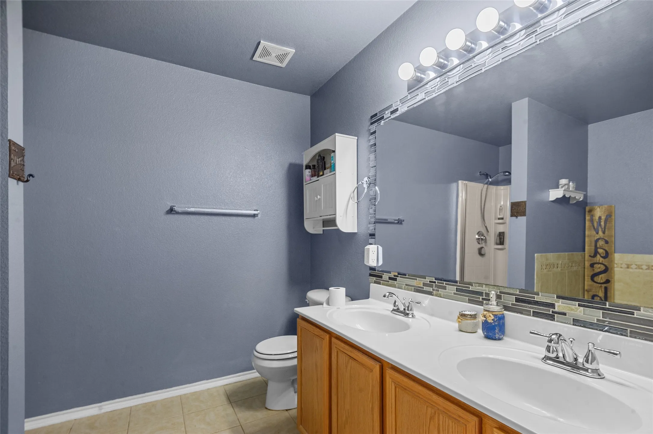 Bathroom with a shower, double vanity, tile patterned floors, and a textured wall