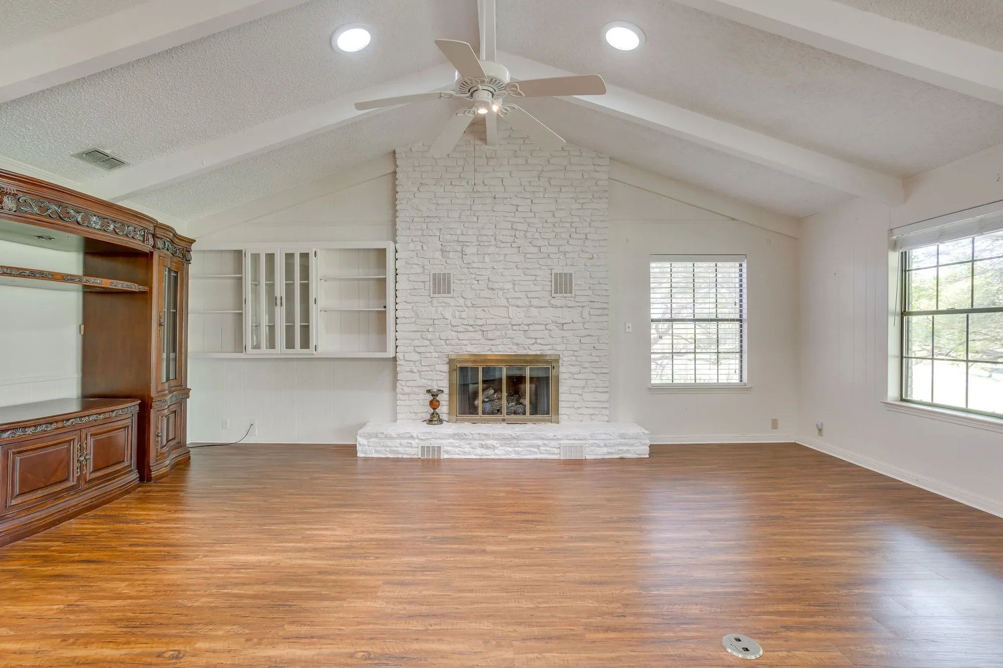 View of the living room featuring a stone fireplace with built-in shelves, sky lights, window across the back.