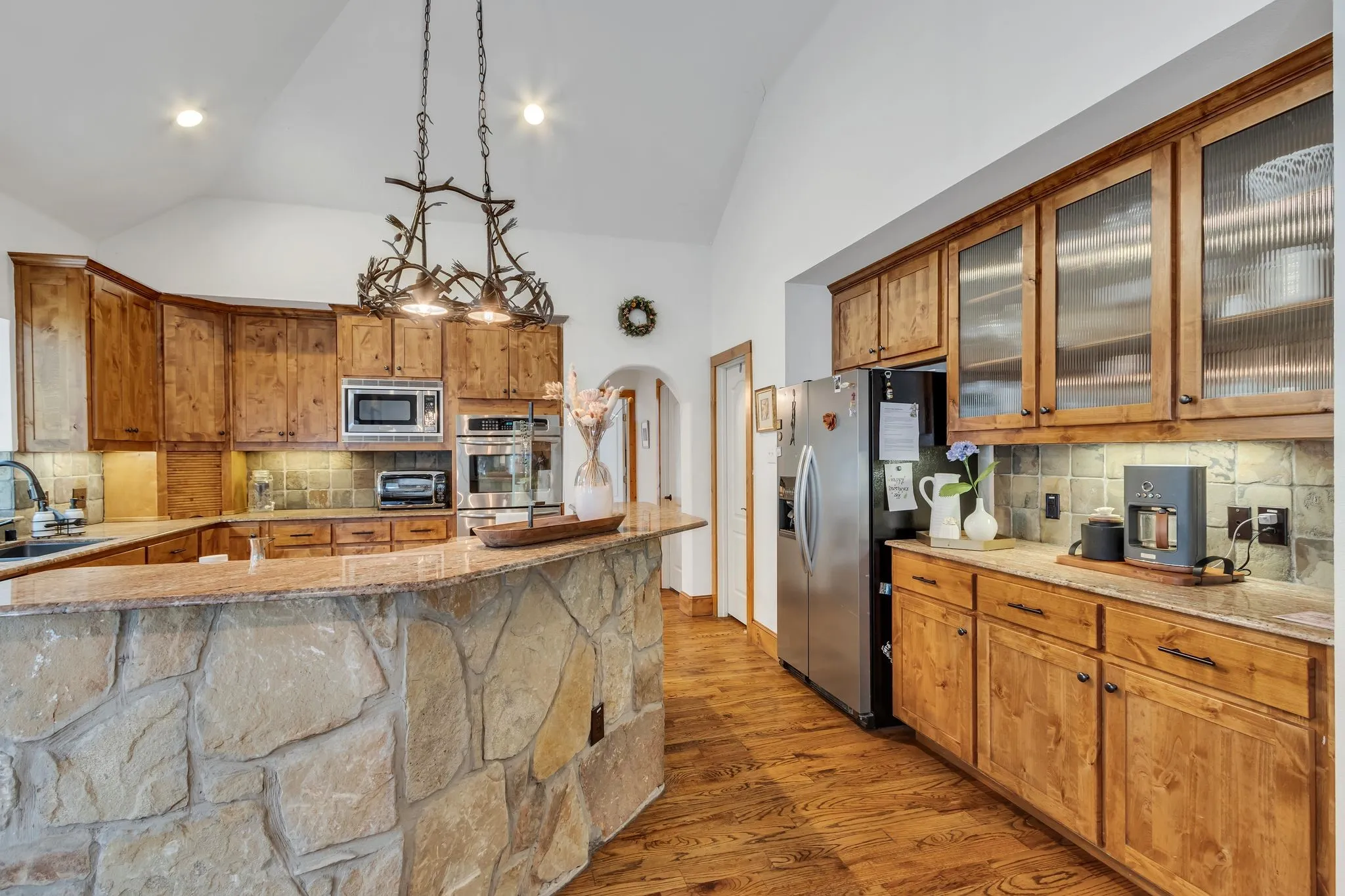 Kitchen featuring a stone-clad breakfast bar, vaulted ceilings, and wood-finish flooring