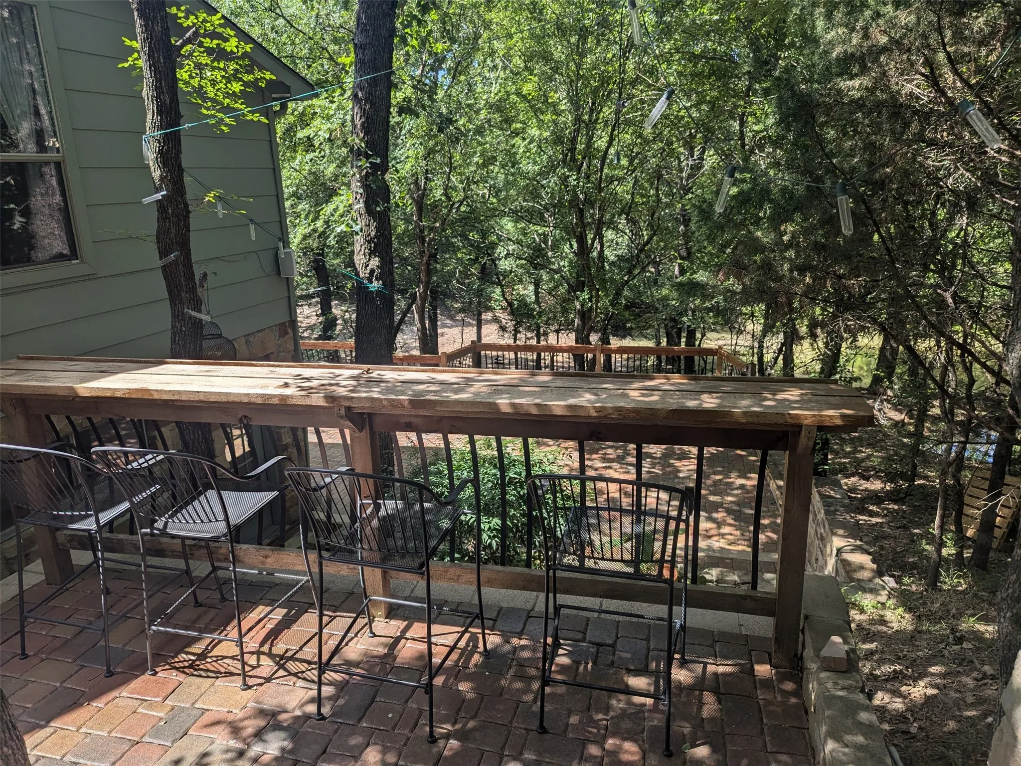 Outdoor entertaining area featuring a wood-finish bar top, brick paver patio, and black metal railings