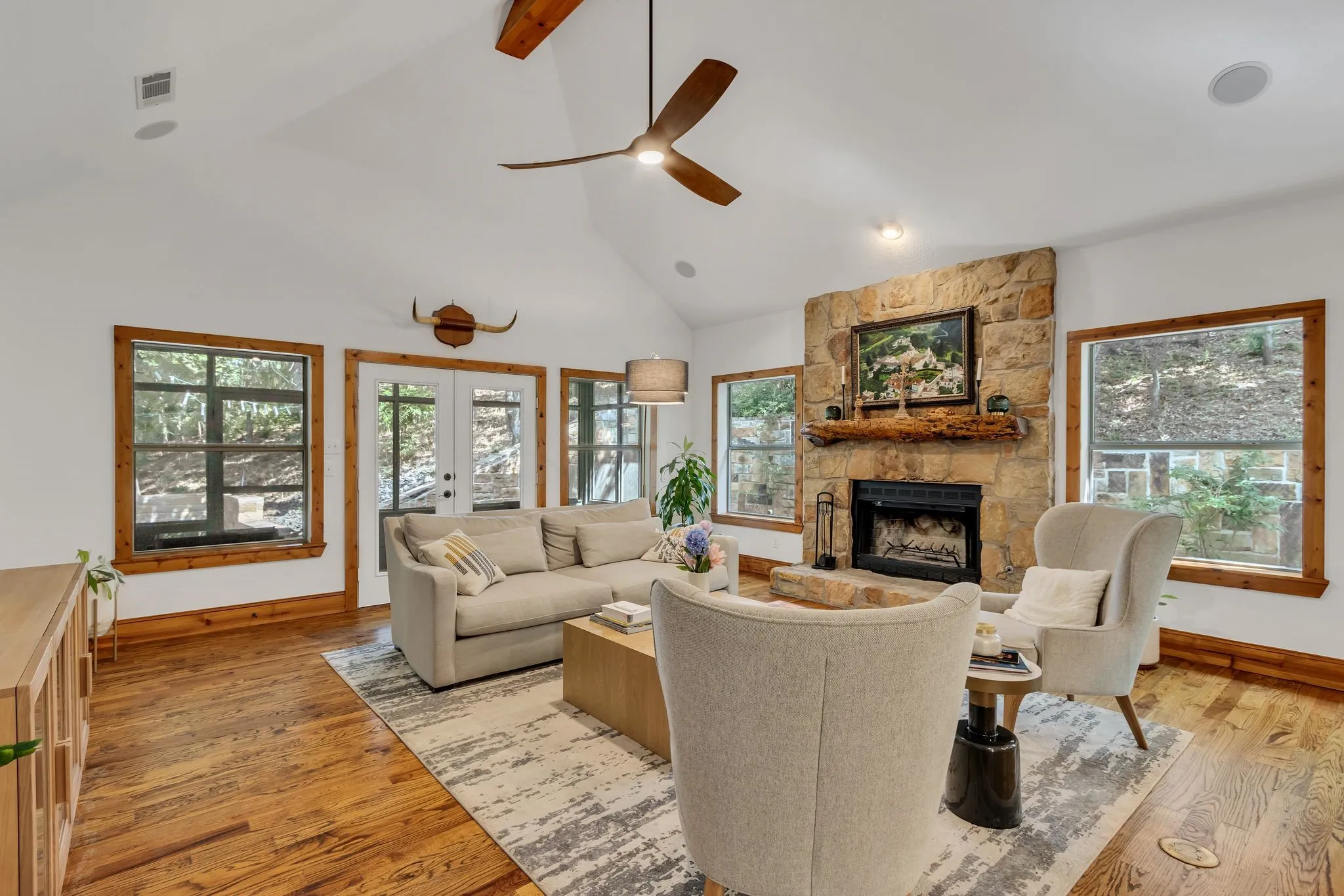 Spacious living area featuring a stone-clad fireplace with a natural wood mantel, wood-finish flooring, and multiple windows