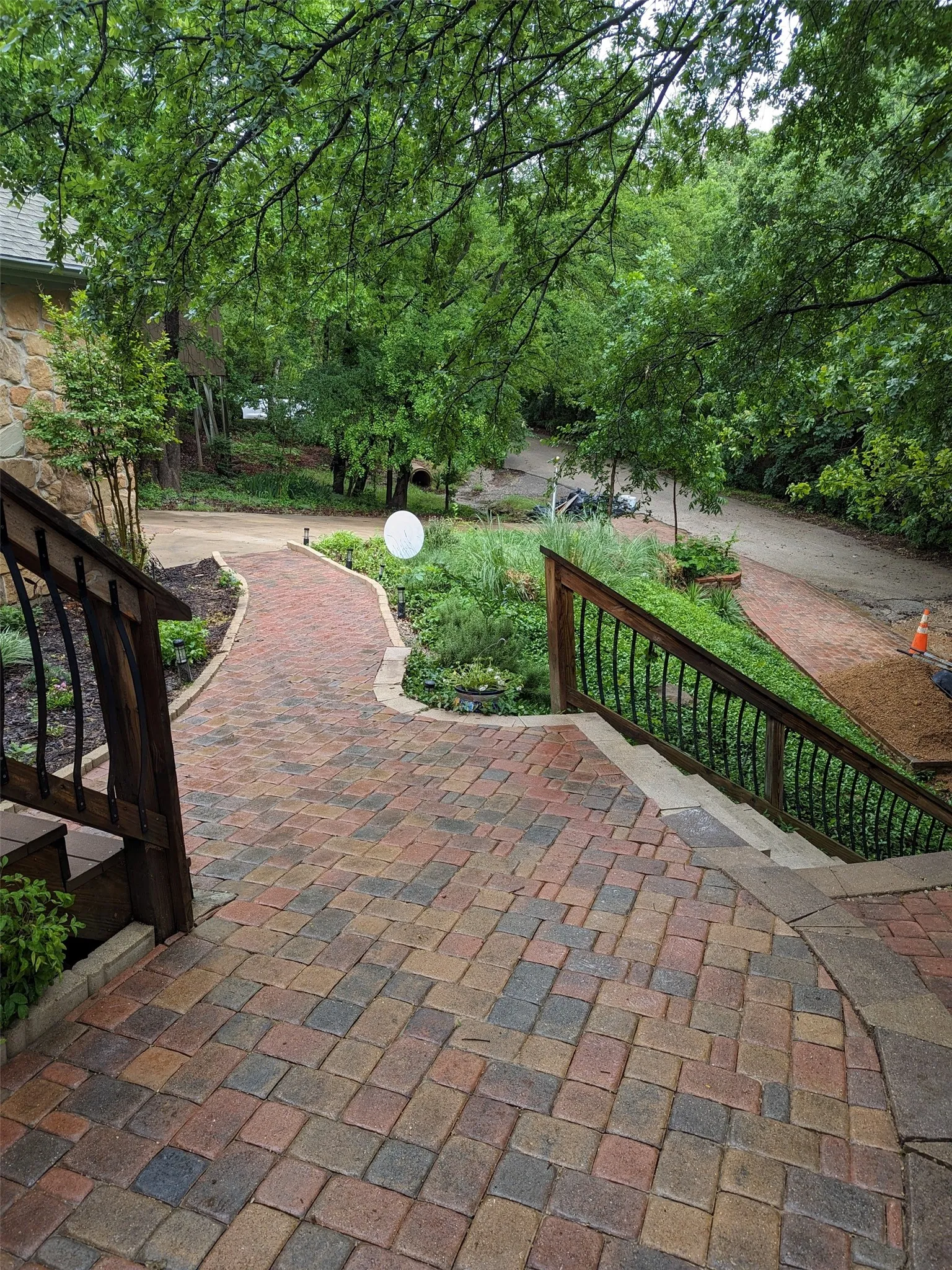 Multi-toned paver stone pathways and steps bordered by dark wood railings and lush landscaping