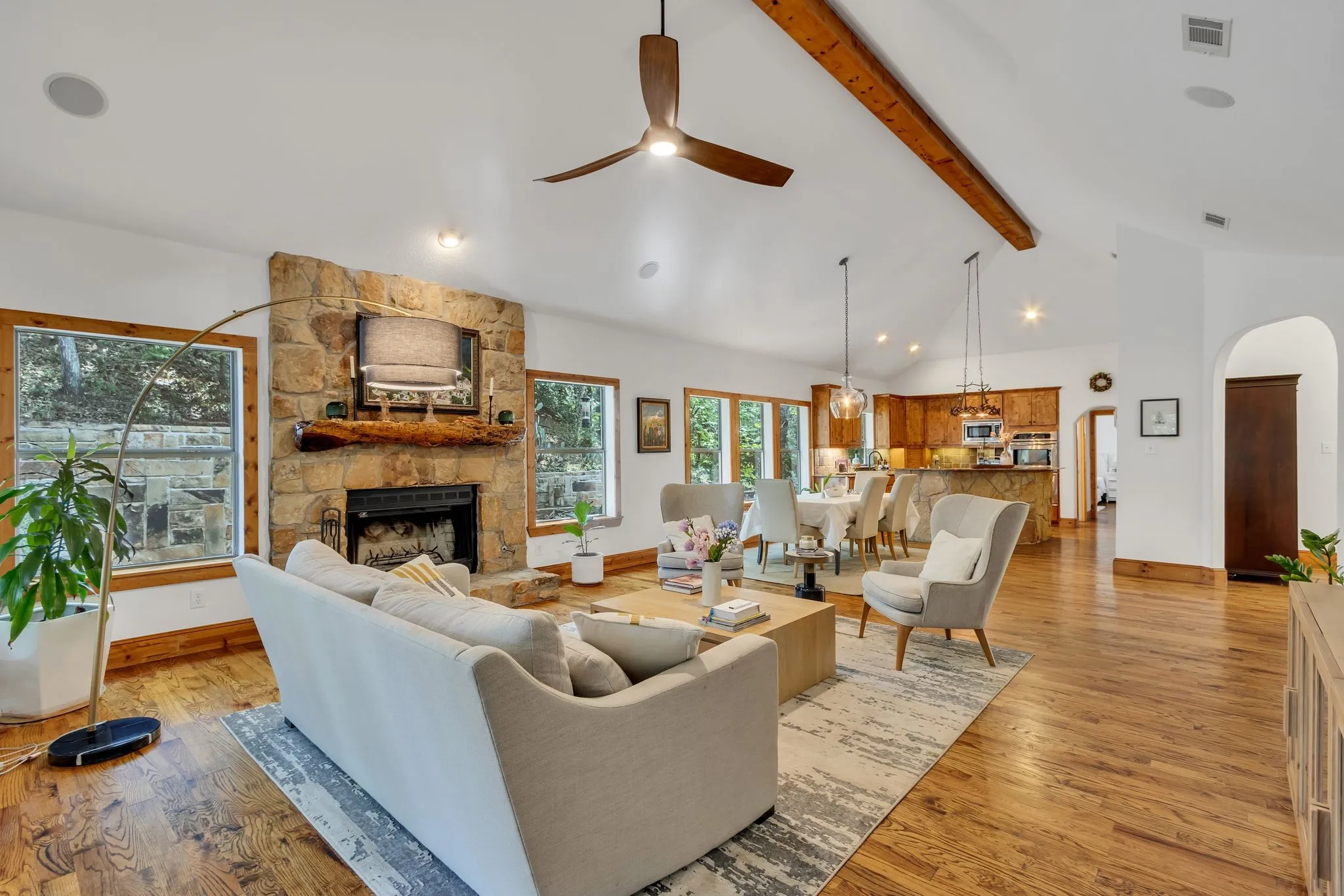 Expansive living area featuring vaulted ceilings with exposed wood beams, a stone fireplace, and wood-finish flooring