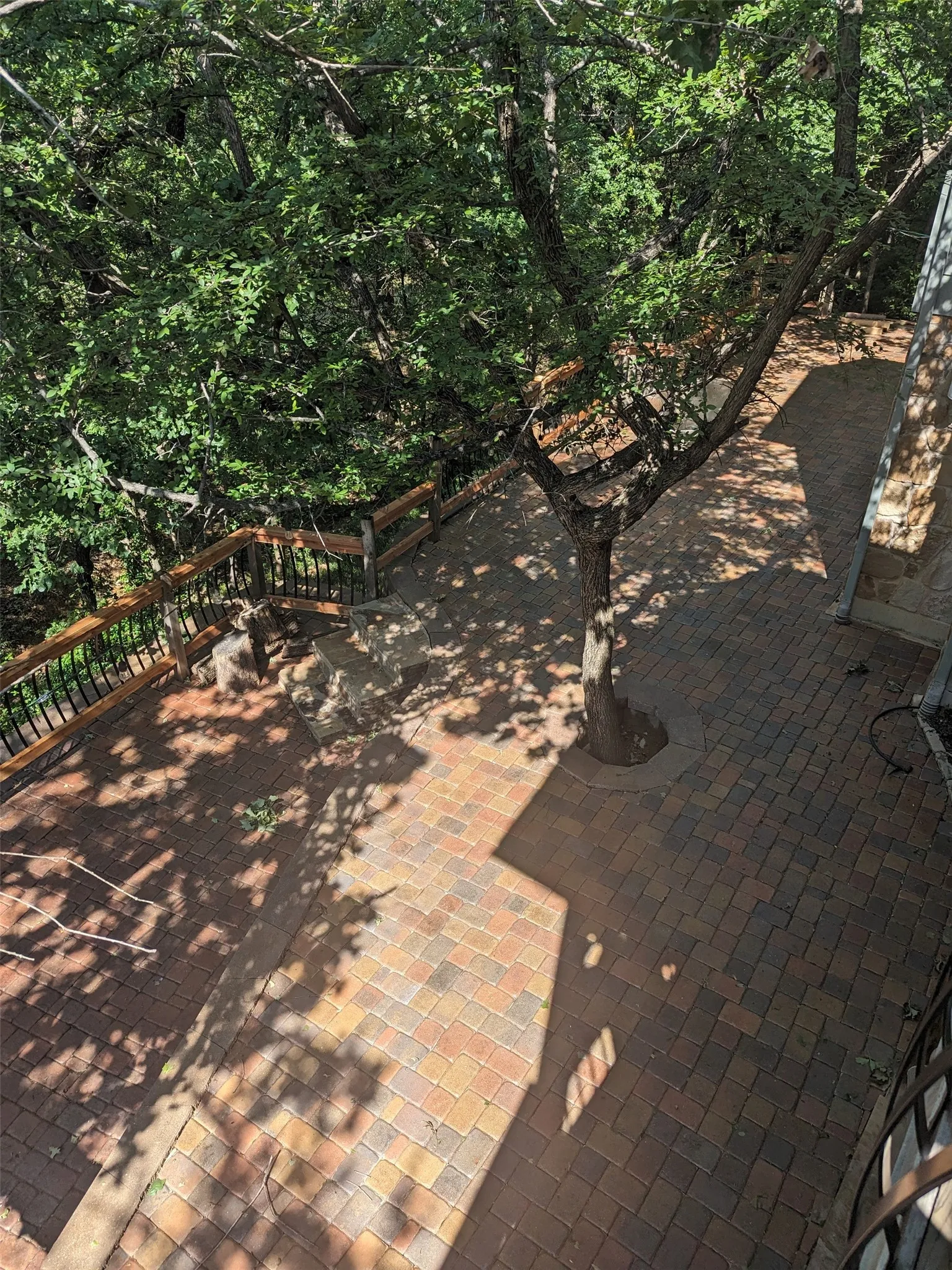 Paver patio area featuring a built-in tree planter and steps with a wood and metal railing