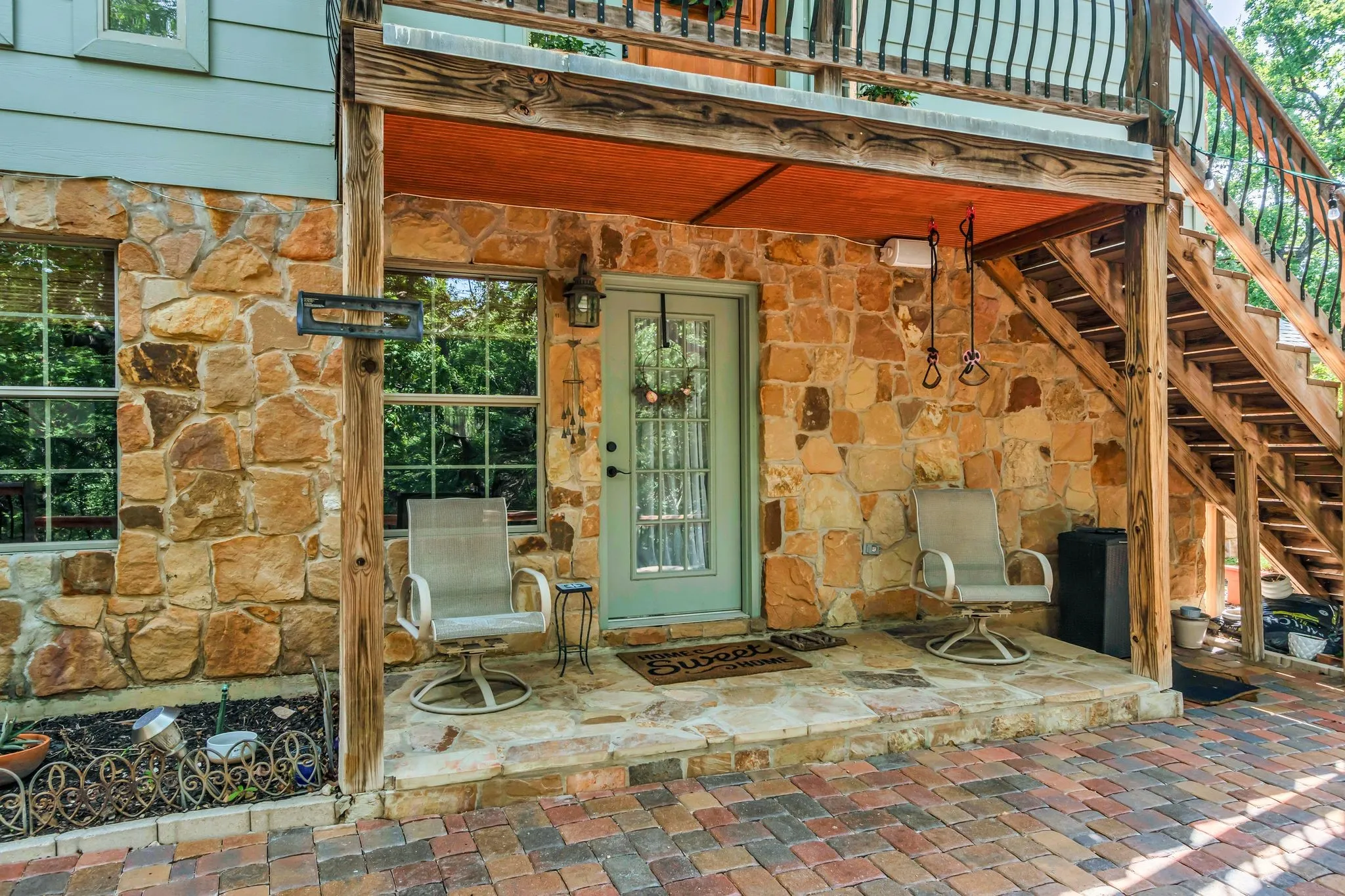 Stone veneer exterior featuring a light blue entry door with glass paneling, a covered patio, and a stone slab porch