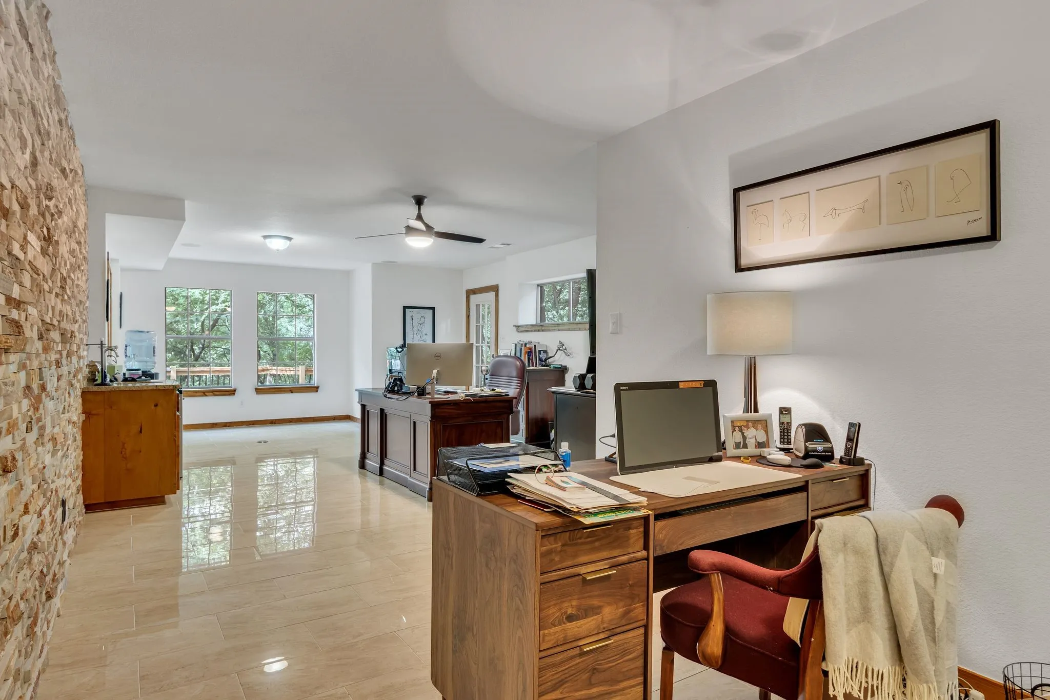 Open concept space featuring light-toned tile flooring, a stacked stone accent wall, recessed lighting, and a ceiling fan