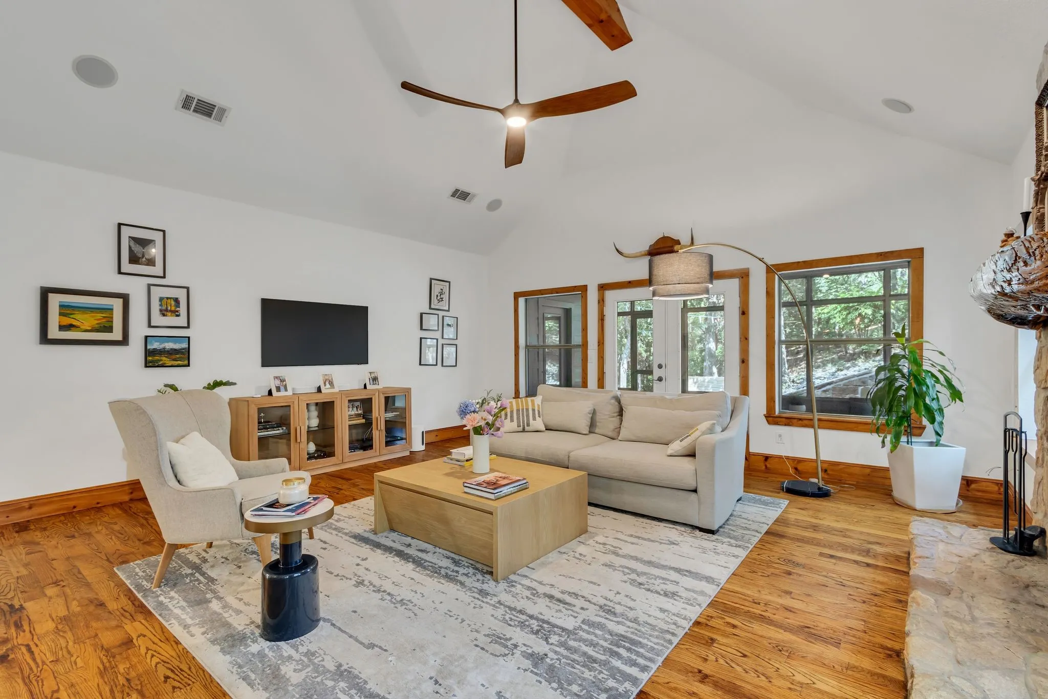 Spacious living area featuring high vaulted ceilings with exposed wood beams, hardwood flooring, and a stone-clad fireplace