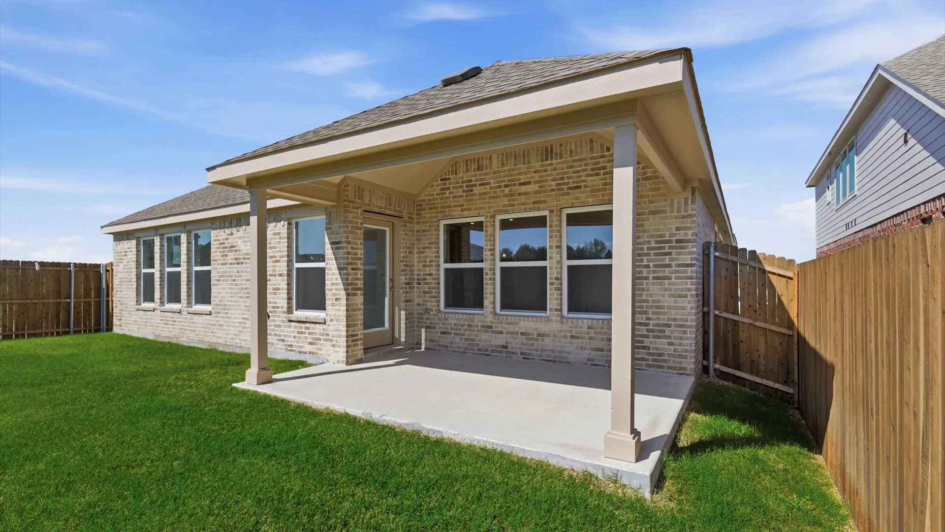 Rear exterior with a covered concrete patio, brick facade, and multiple windows
