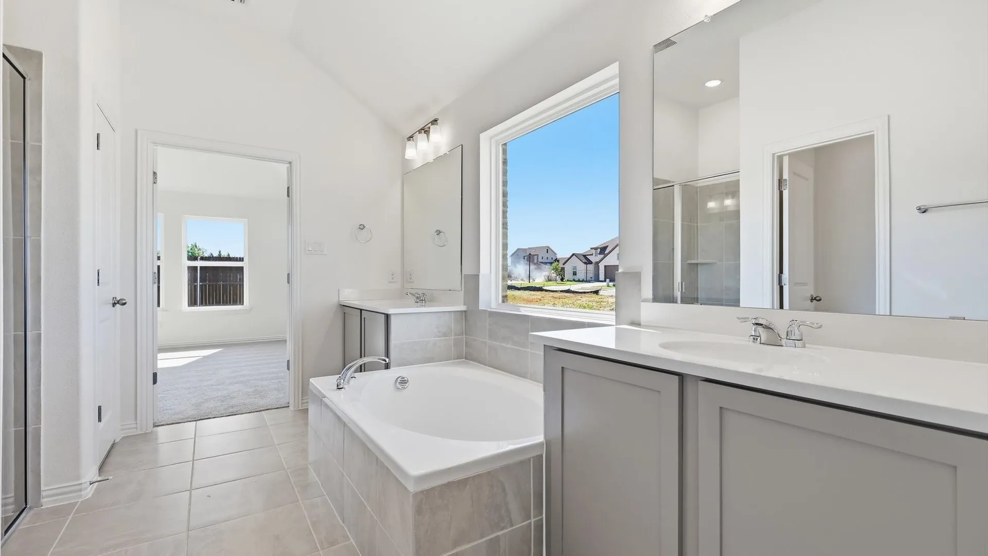 Contemporary bathroom featuring a built-in soaking tub, dual vanities with white countertops, and a large window