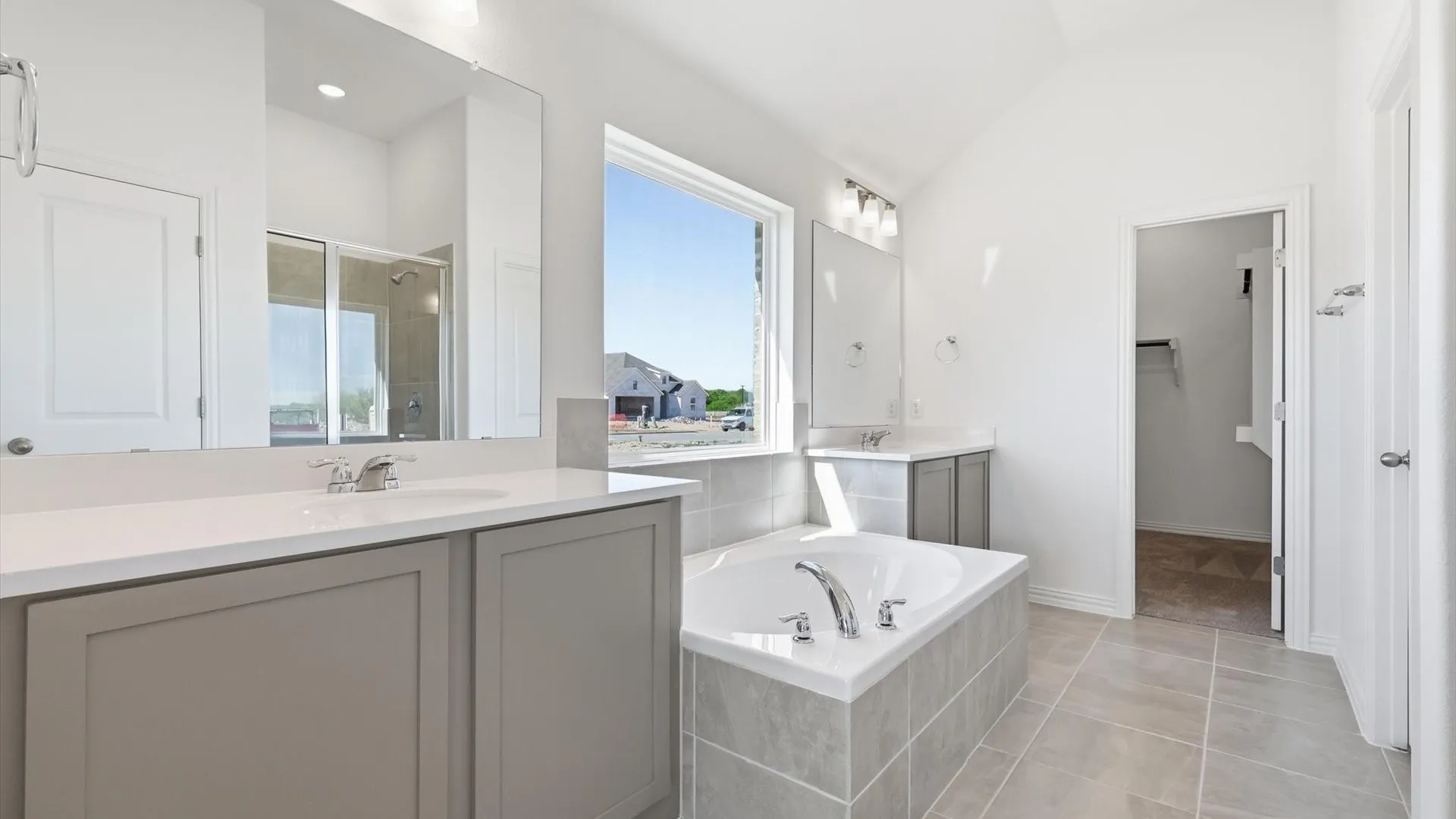 Spacious bathroom featuring a built-in soaking tub with tiled surround, dual vanities with integrated sinks, and ample natural light from a large window