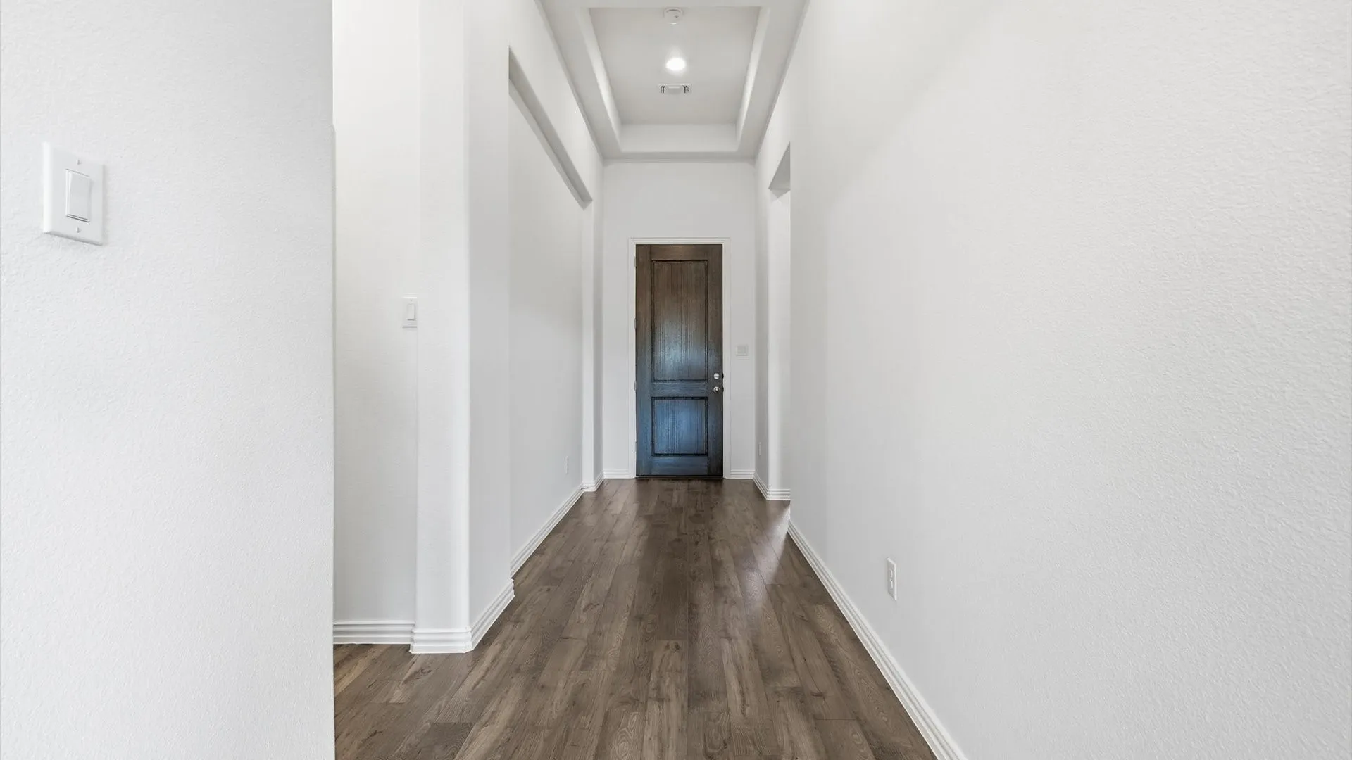 Hallway featuring wood-finish flooring, white baseboards, recessed lighting, and a dark wood door