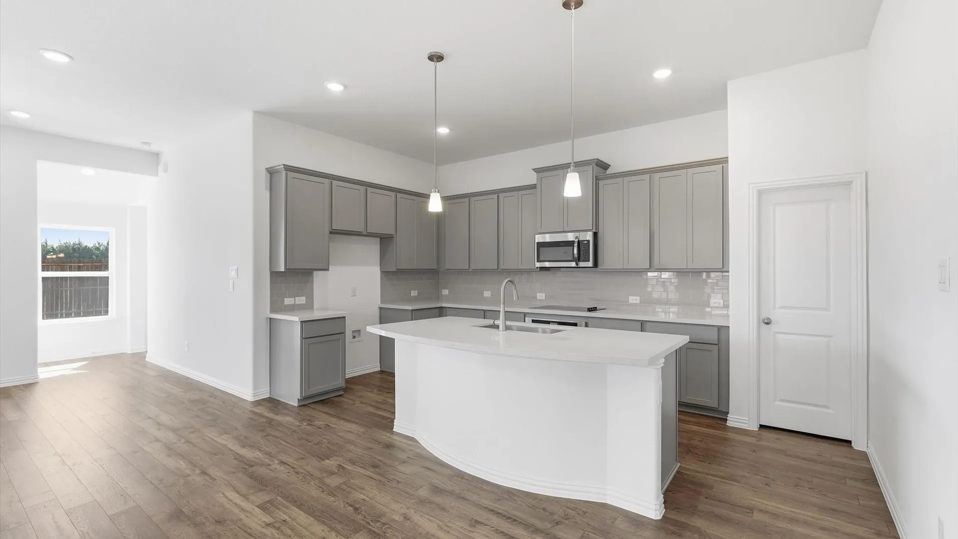 Open-concept kitchen featuring an island with an undermount sink, pendant lighting, stainless steel microwave, grey cabinetry, and wood-finish flooring