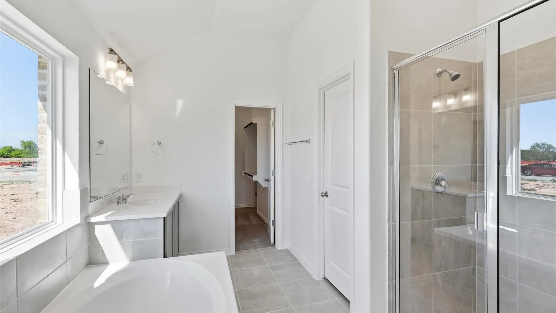Bright bathroom featuring a glass-enclosed shower with integrated bench seating, a separate soaking tub, a single vanity with an undermount sink and stone-finish countertop, and tiled flooring