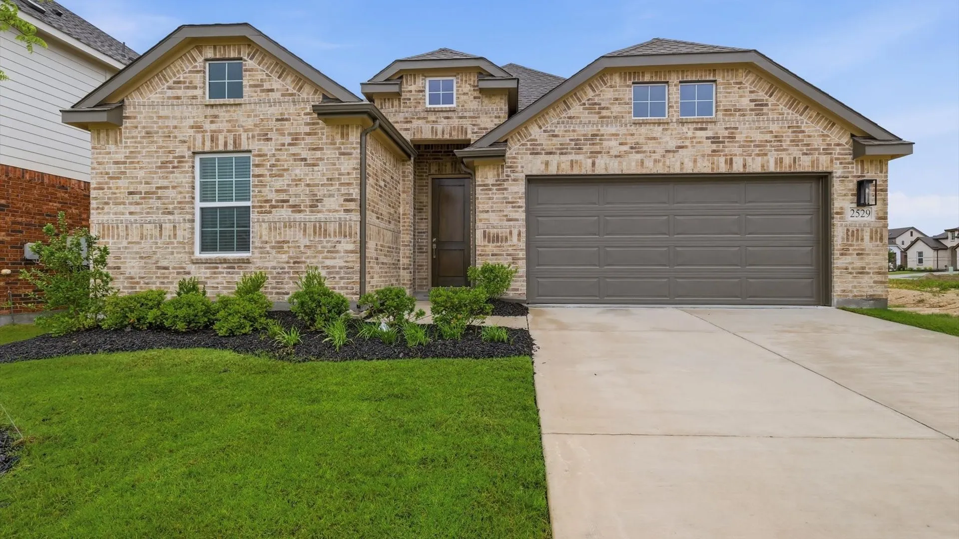 Brick facade featuring a two-car garage, concrete driveway, and manicured lawn