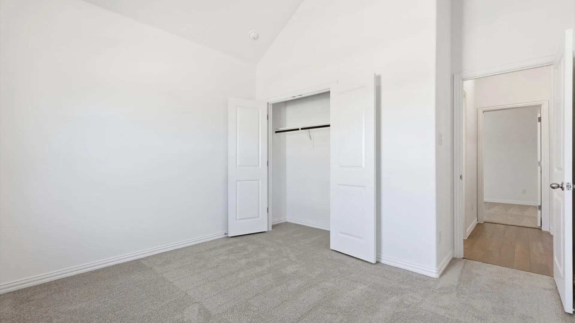 Room featuring a vaulted ceiling, light gray carpet flooring, white baseboards, and a bi-fold closet with a hanging rod