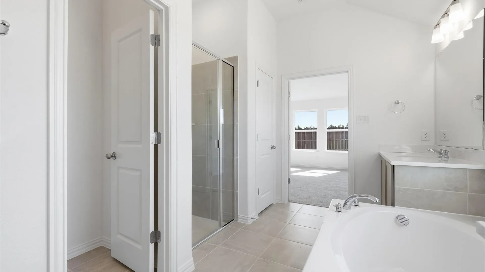 Spacious bathroom featuring a built-in soaking tub with deck-mounted fixtures, a glass-enclosed shower, a double vanity with stone countertops, and tile flooring