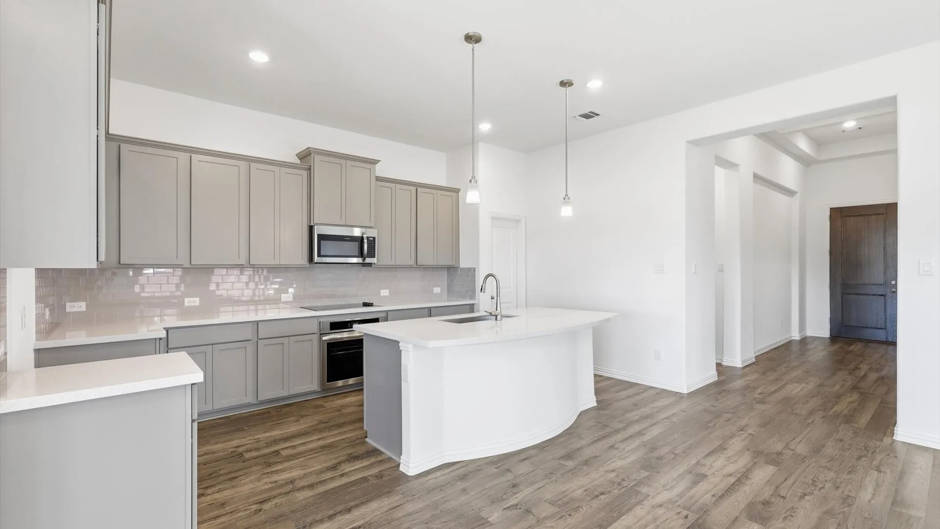 Open-concept kitchen featuring an arc-shaped island with an undermount sink, pendant lighting, shaker-style cabinetry, a subway tile backsplash, and wood-finish flooring