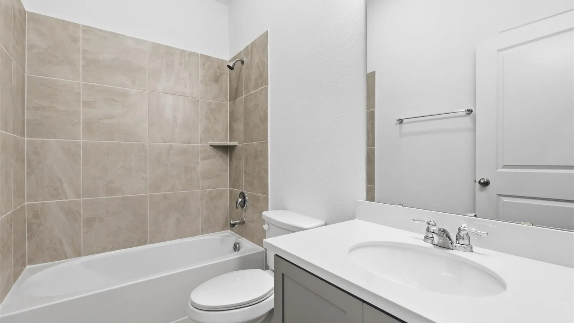 Bathroom featuring a built-in tub with tile surround, a built-in shower niche, a single vanity with an integrated sink, a light-toned countertop, and a mirrored wall