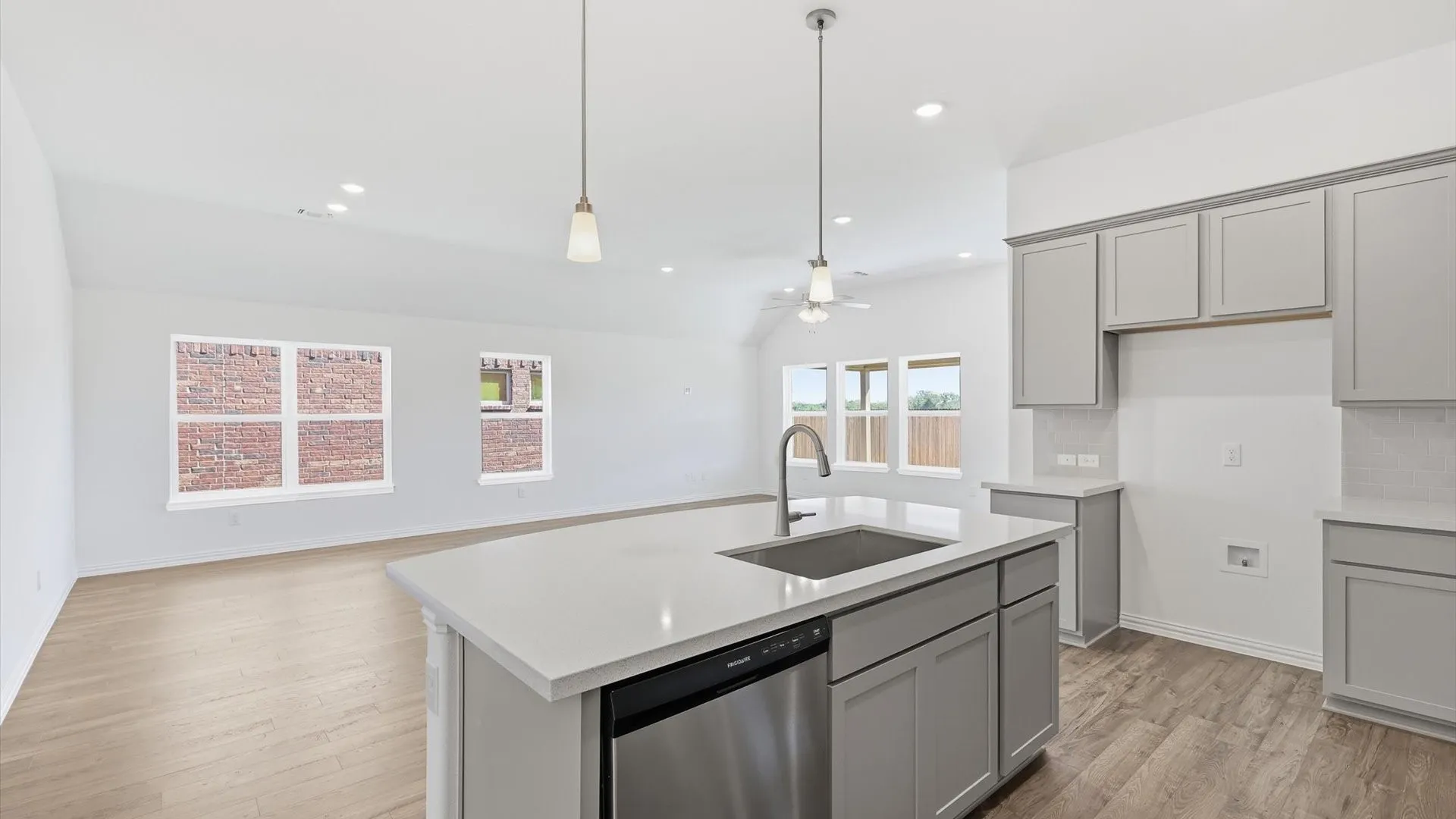 Open-concept kitchen featuring a large island with sink, stainless steel dishwasher, pendant lighting, shaker-style cabinetry, and light-toned countertops