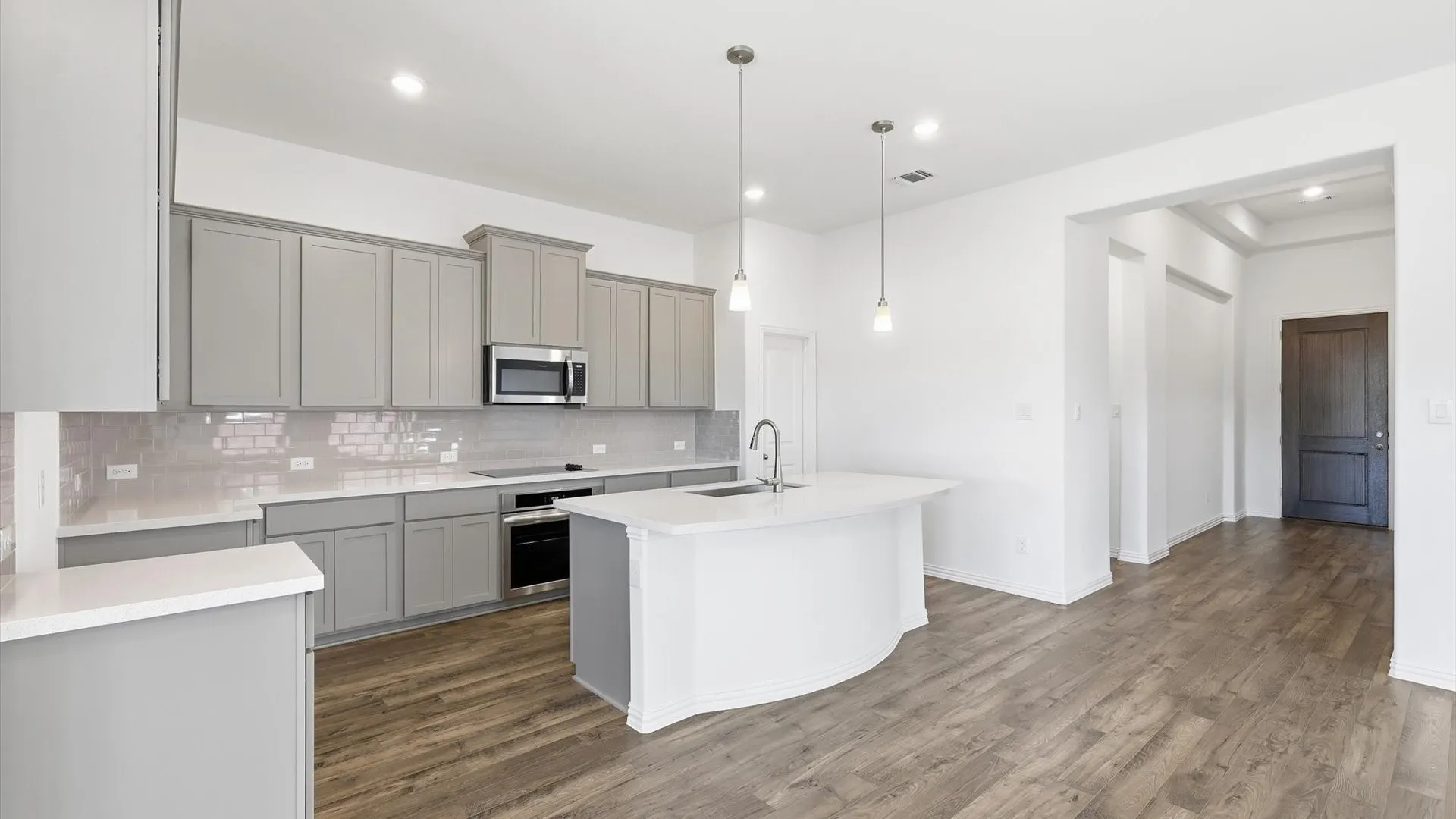 Contemporary kitchen with light grey cabinetry, white countertops, stainless steel appliances, and a curved island featuring pendant lighting