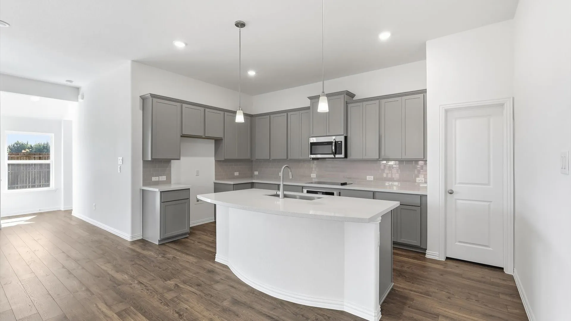 Modern kitchen featuring a curved island with integrated sink, stainless steel appliances, grey cabinetry, light-toned countertops, and wood-finish flooring