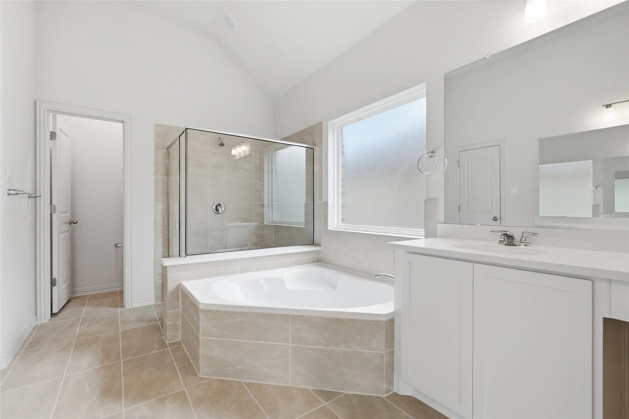 Spacious bathroom featuring a corner soaking tub, glass-enclosed shower, dual vanity with white cabinetry, large vanity mirror, and vaulted ceiling
