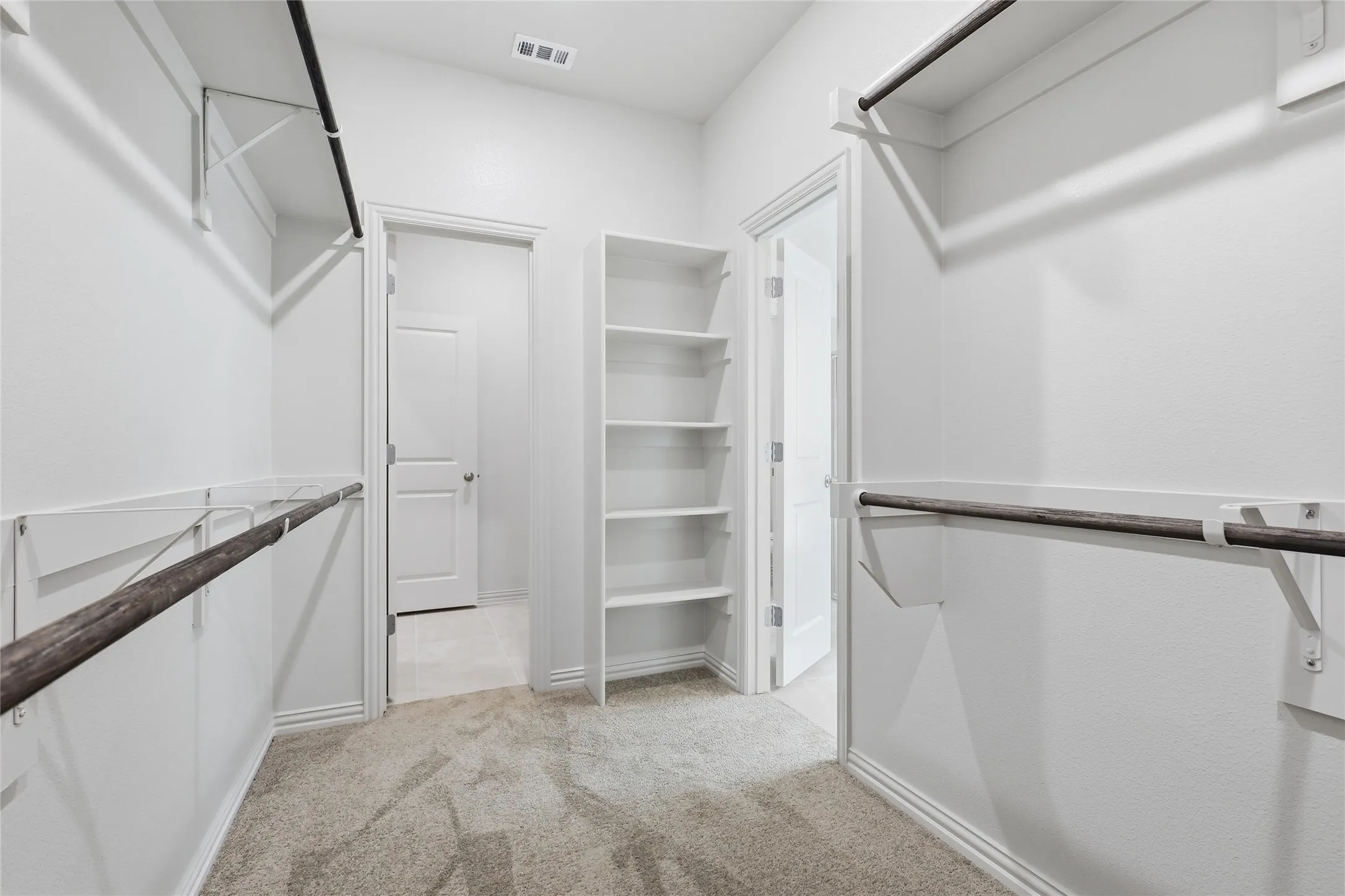Walk-in closet featuring carpet flooring, built-in shelving, two hanging rods, and bright white walls
