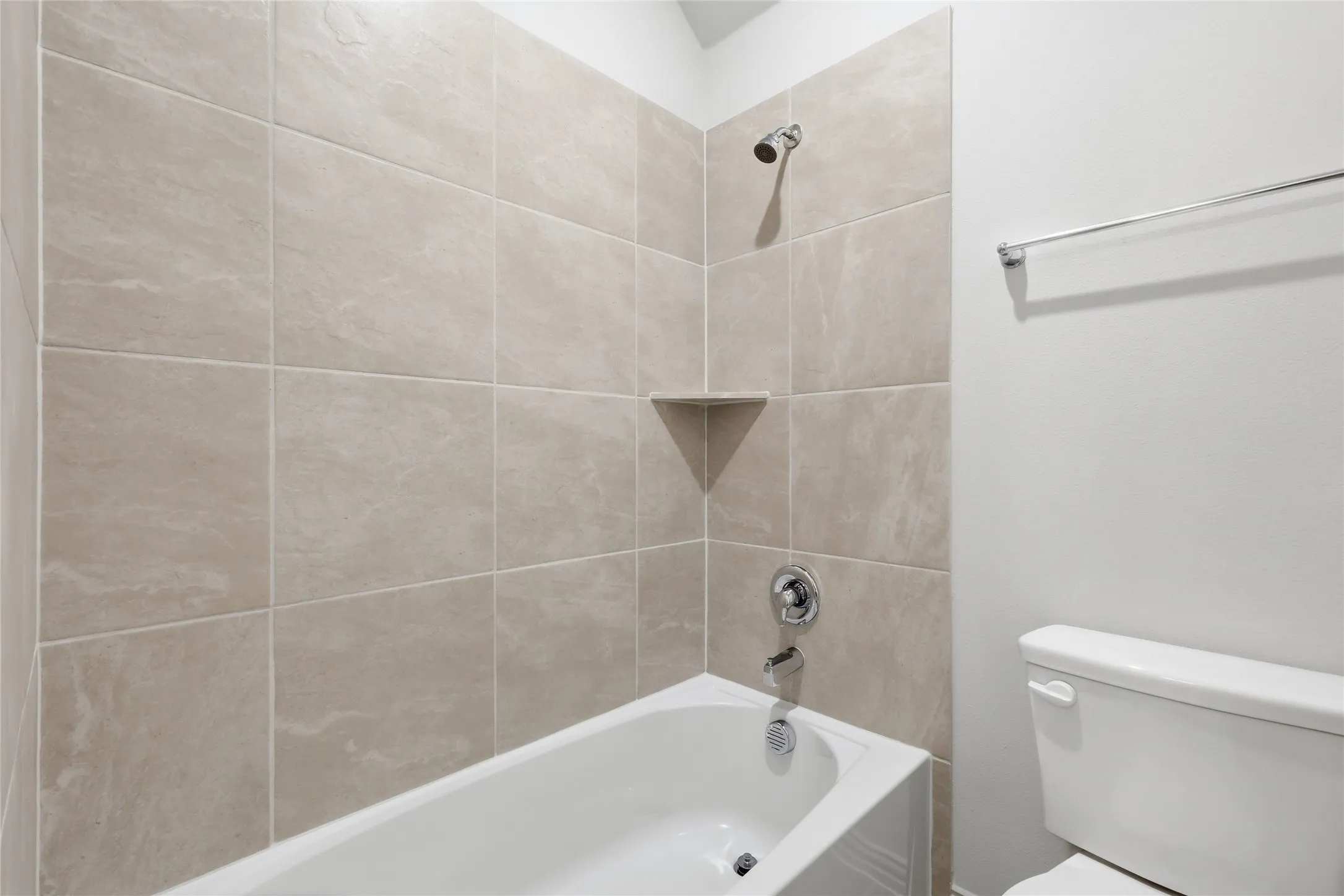 Bathtub and shower combination featuring neutral-toned tile surround with a corner shelf