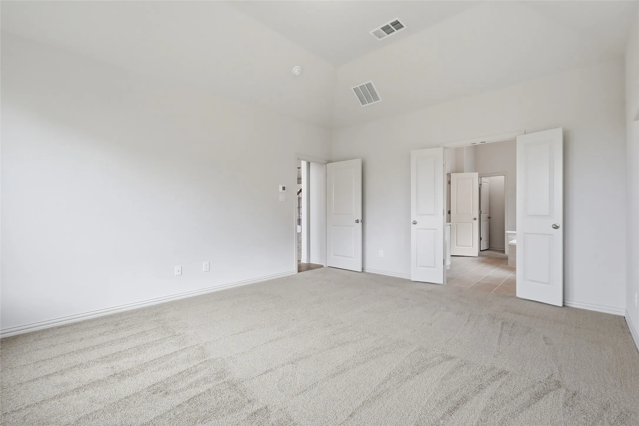 Spacious carpeted room featuring a vaulted ceiling and multiple white panel doors