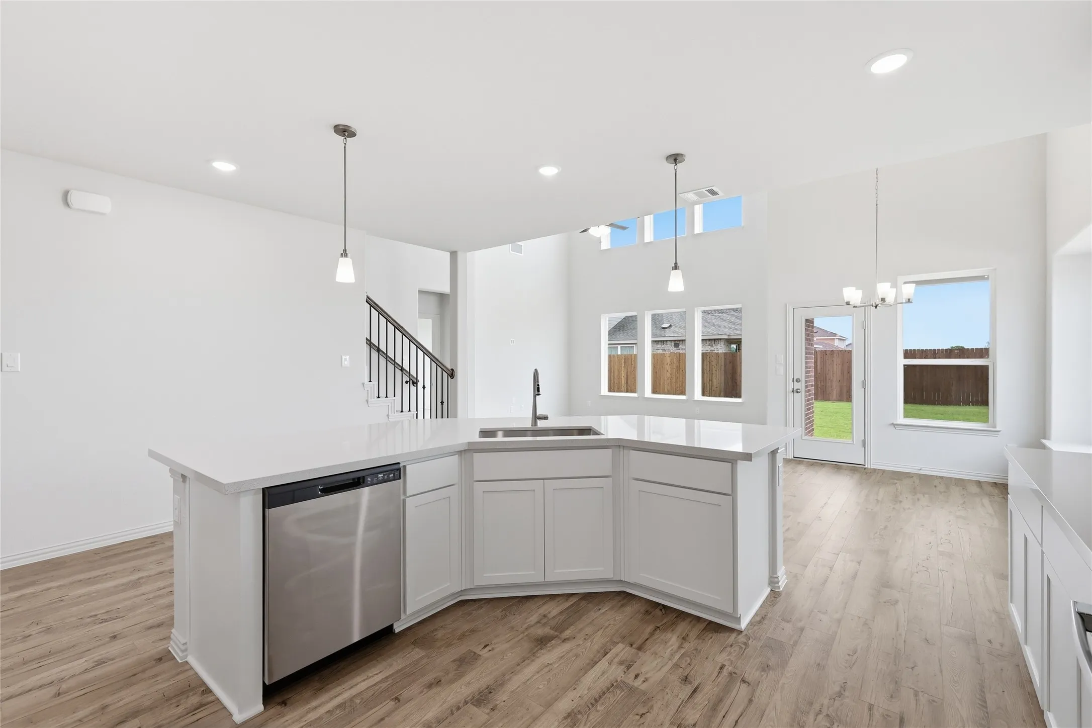Spacious kitchen island featuring a stainless steel dishwasher, undermount sink with a gooseneck faucet, and two pendant lights