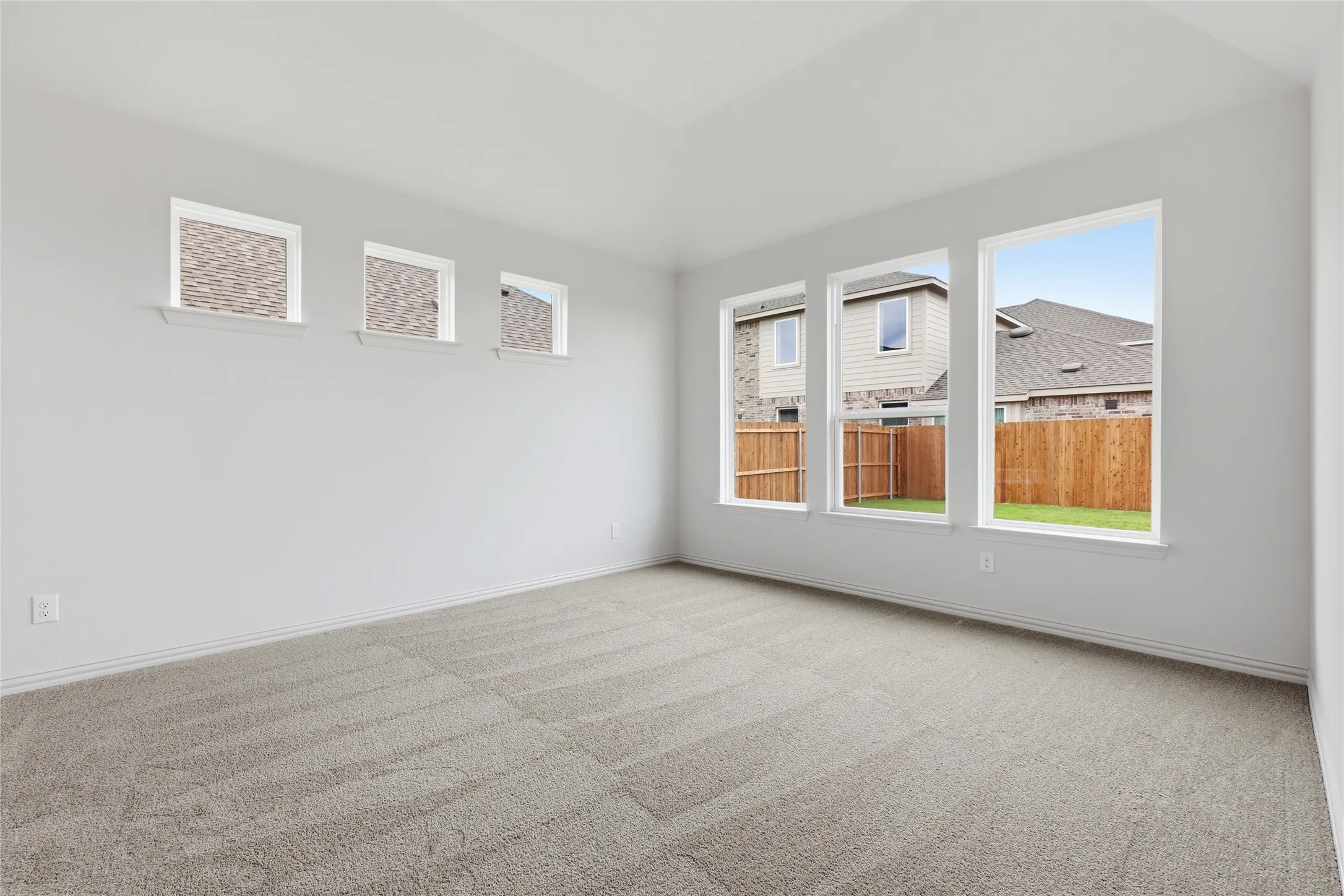 Spacious room featuring neutral carpeting, light-toned walls, and multiple windows