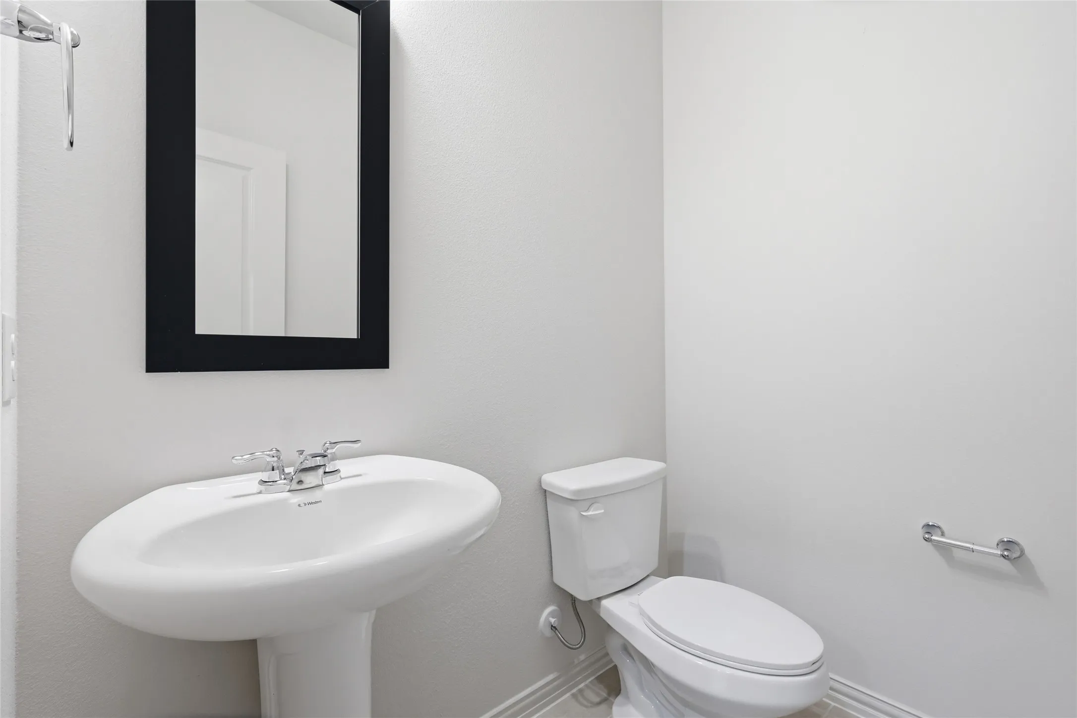 Pedestal sink with chrome faucet, complemented by a rectangular framed mirror and a modern toilet