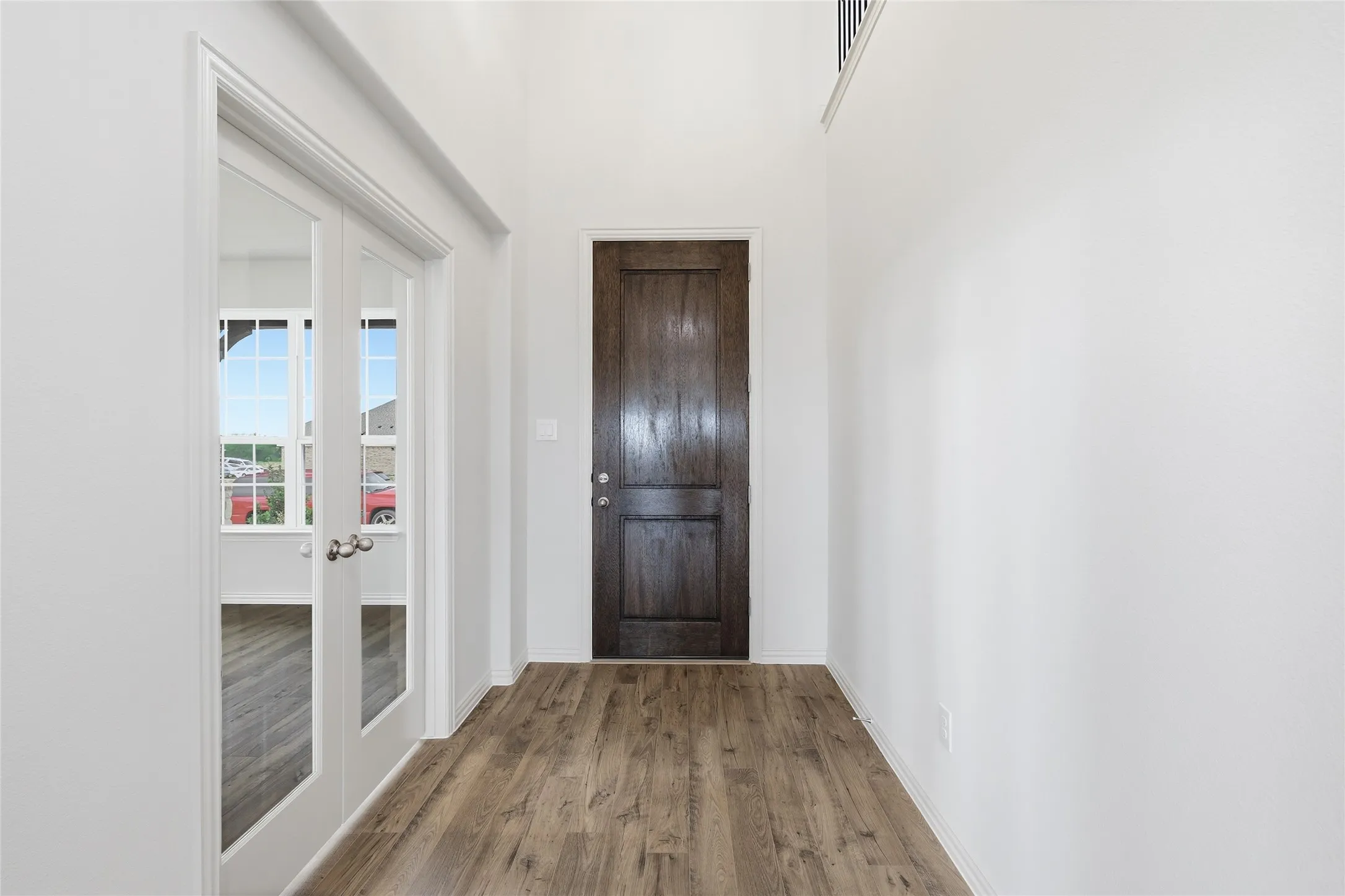 Entryway featuring wood-finish flooring, a dark wood paneled door, and tall white walls