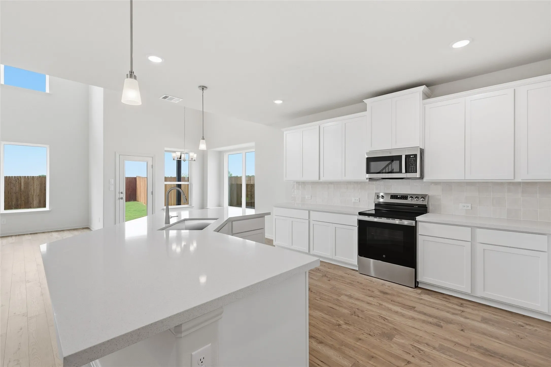 Open-concept kitchen featuring an expansive island with a sink, white cabinetry, a subway tile backsplash, and stainless steel appliances