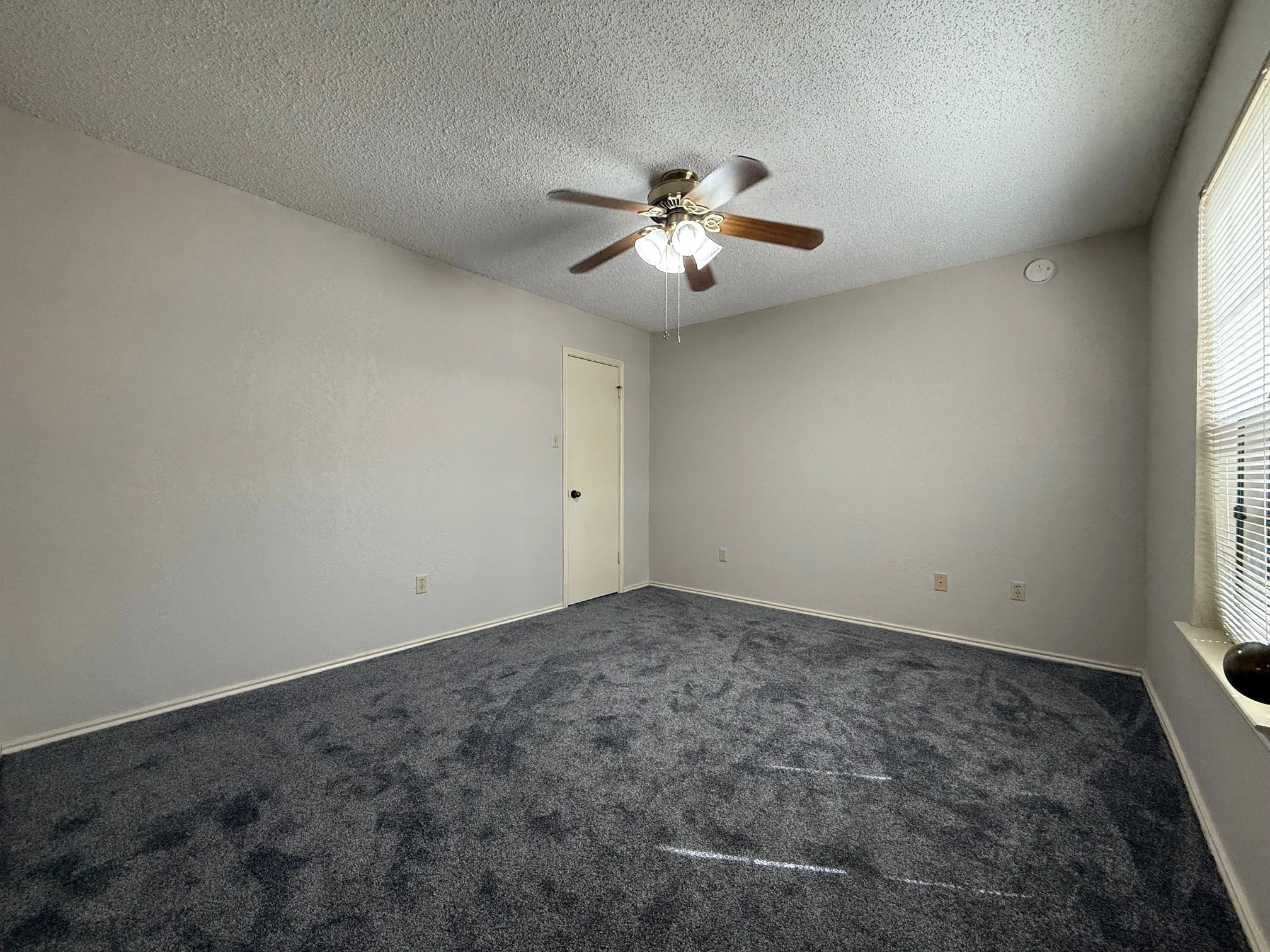 Unfurnished room with dark carpet, ceiling fan, and a textured ceiling