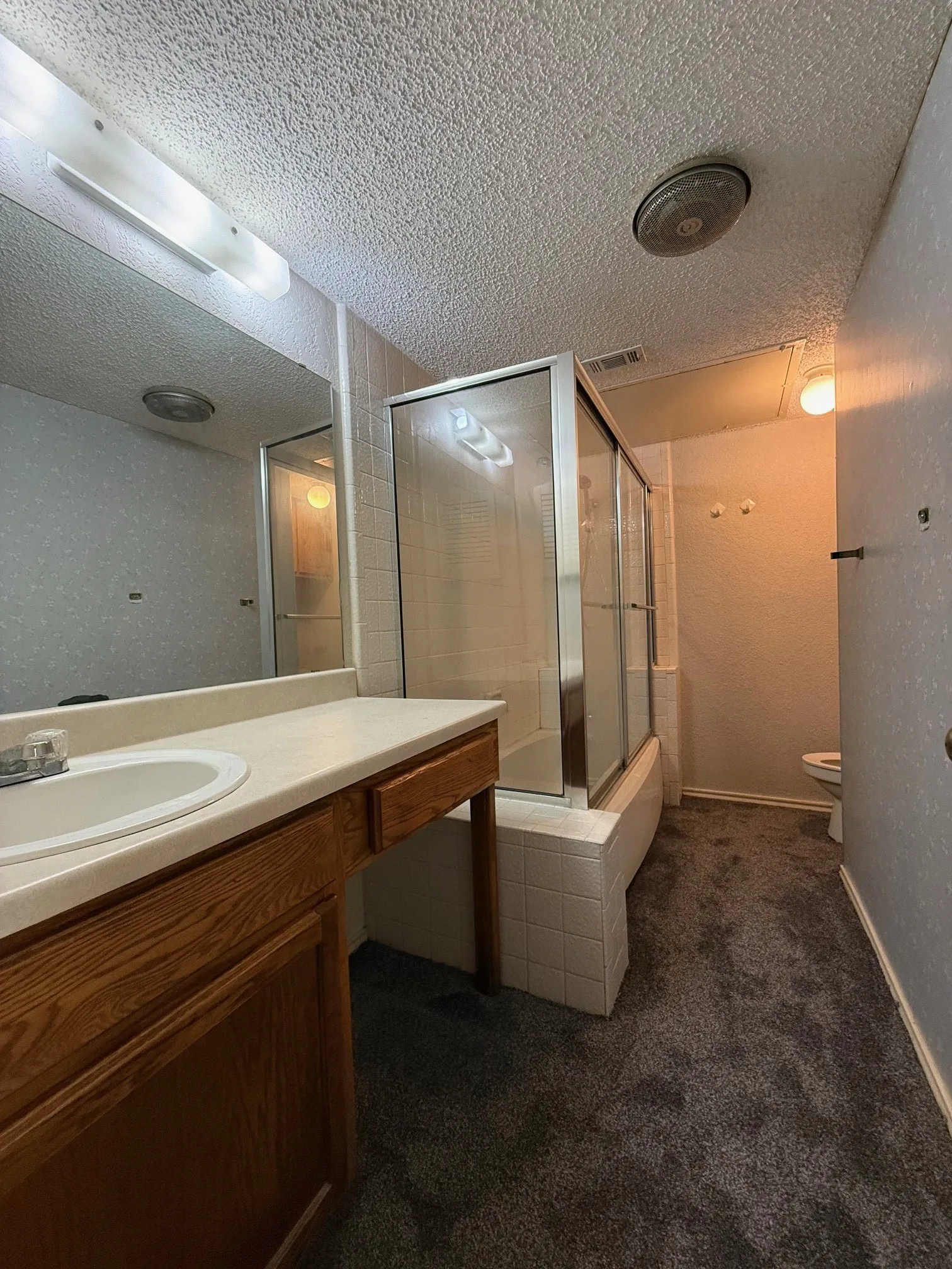 Bathroom with dark colored carpet, vanity, a textured ceiling, and bath / shower combo with glass door
