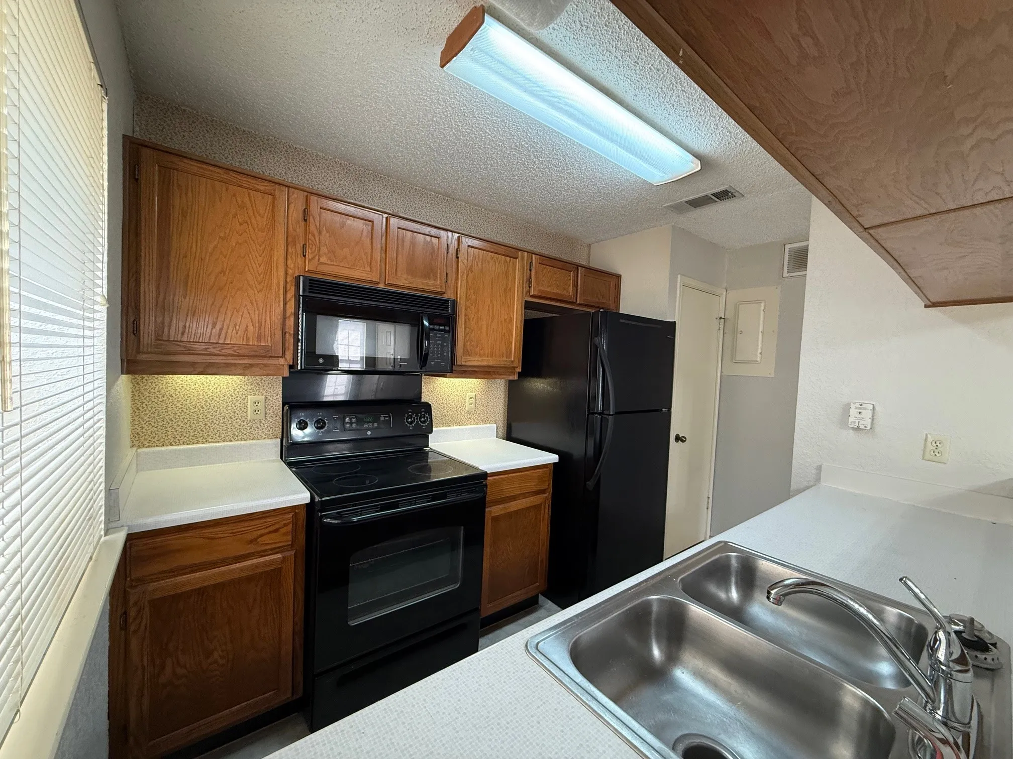 Kitchen with black appliances, wood finish cabinets, light countertops, and a textured ceiling