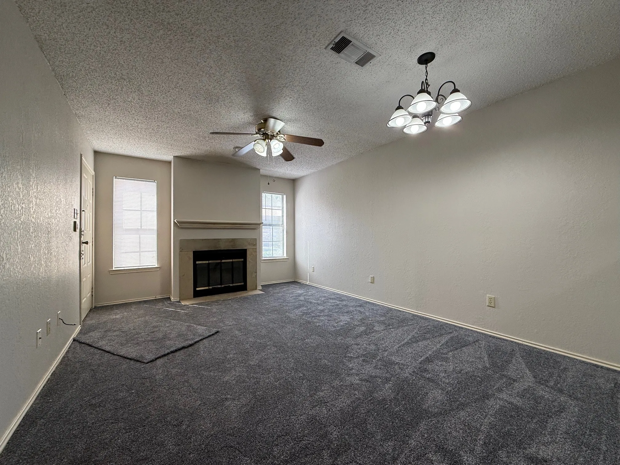 Unfurnished living room with a textured wall, dark colored carpet, ceiling fan, a fireplace, and a textured ceiling