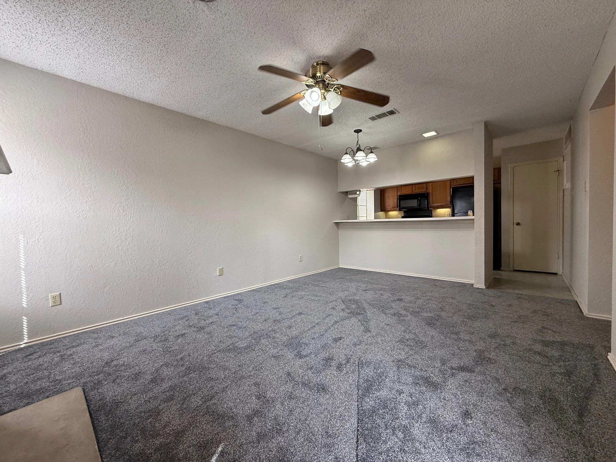 Unfurnished living room featuring ceiling fan, dark colored carpet, a chandelier, a textured ceiling, and a textured wall