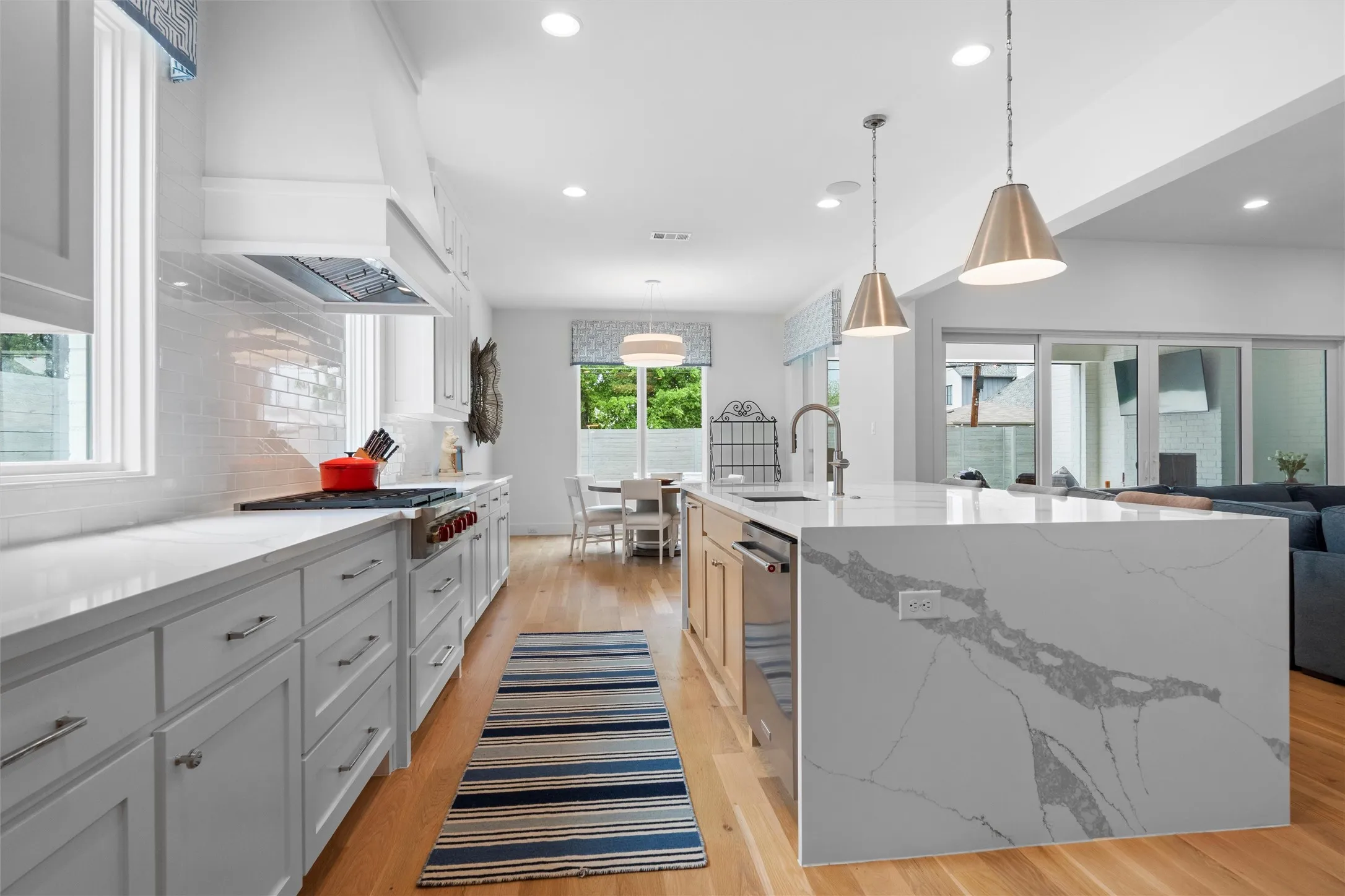Kitchen featuring hanging light fixtures, tasteful backsplash, light hardwood / wood-style floors, and an island with sink.