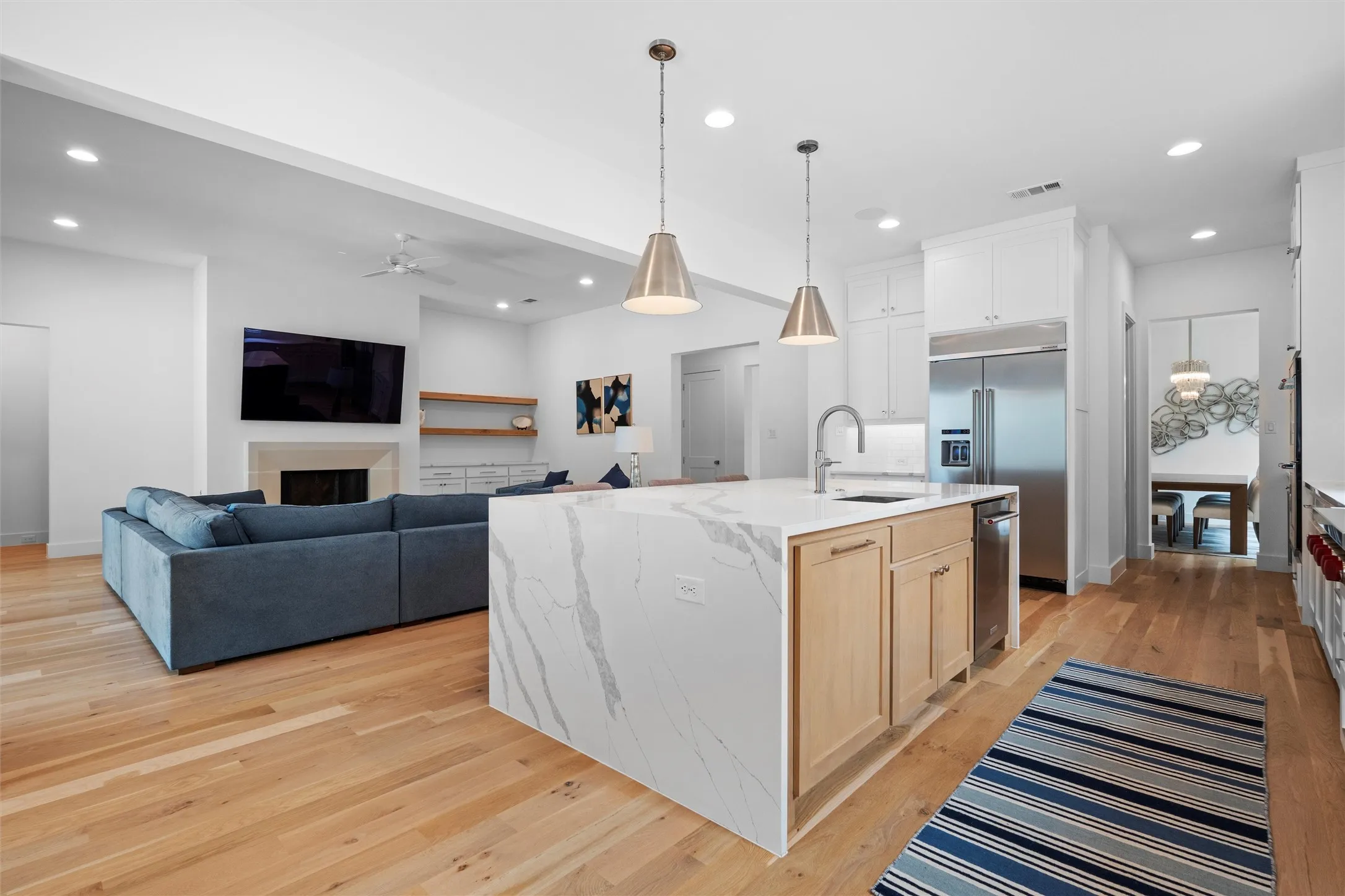 A view from the breakfast room, looking into the kitchen and living room.  Kitchen featuring a center island with sink, pendant lighting, and light wood-type flooring