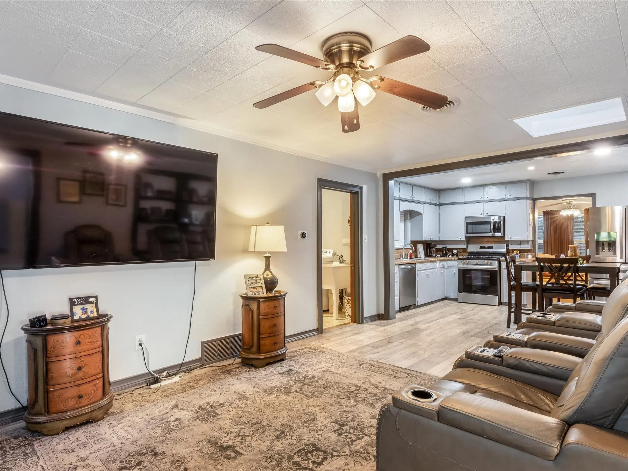 Living room featuring light wood-style floors, a ceiling fan, and a skylight