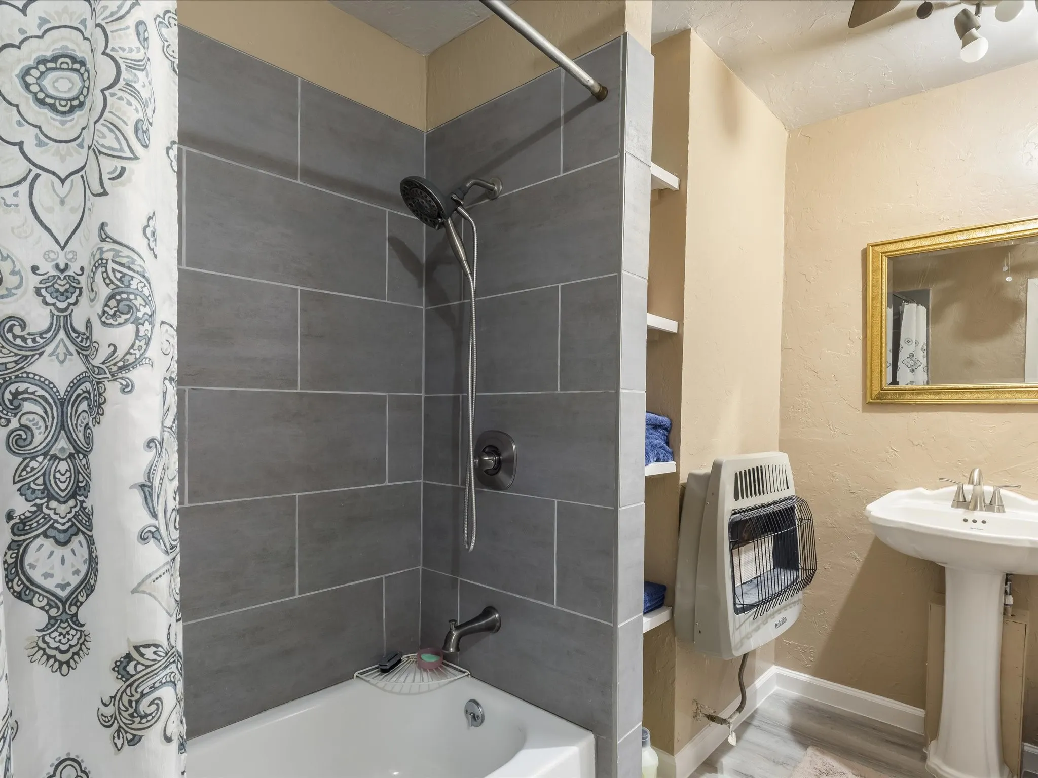 Full bath with a textured wall, heating unit, and shower / tub combo